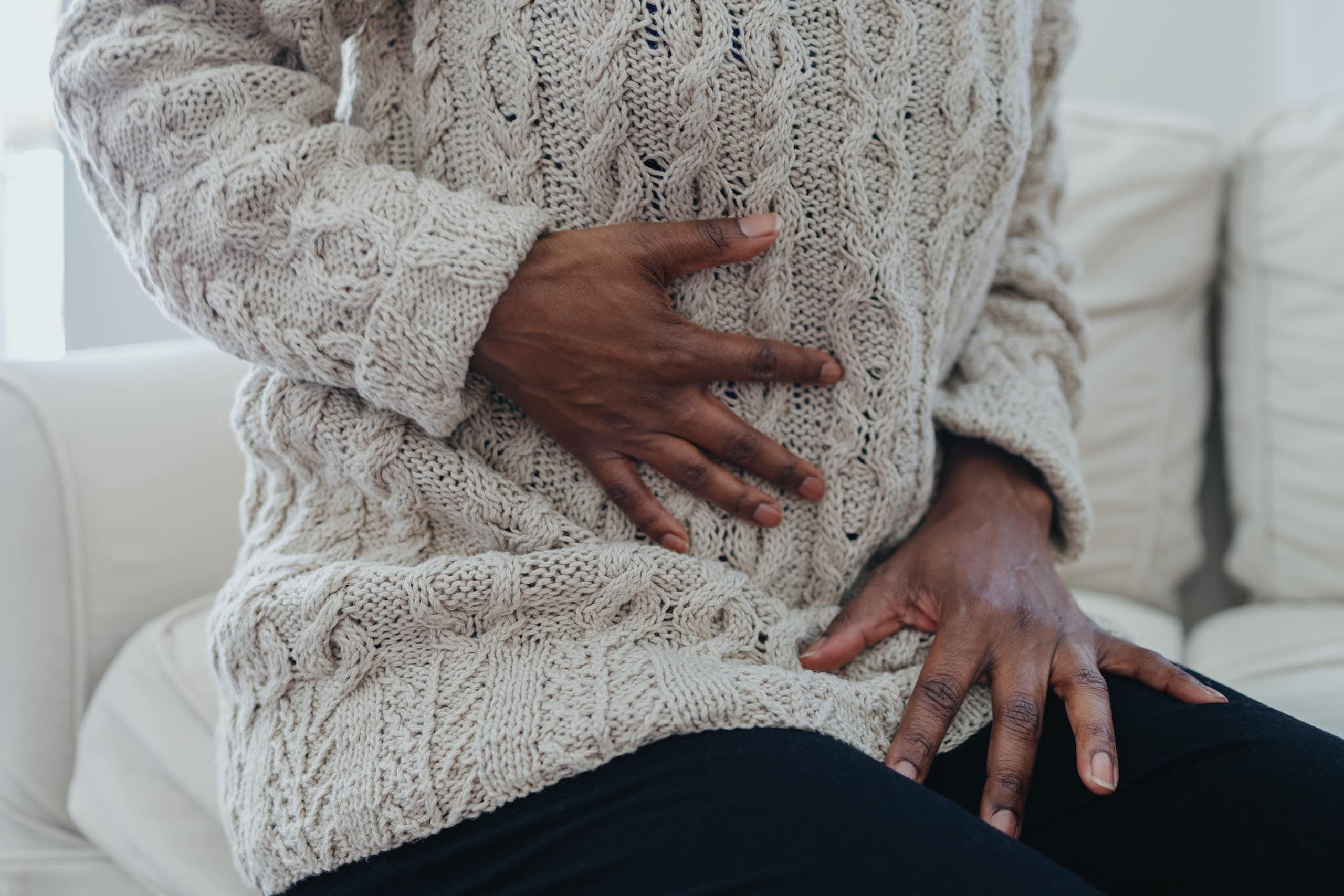 A hand clutching at the stomach as if in pain while the other grips the thigh.