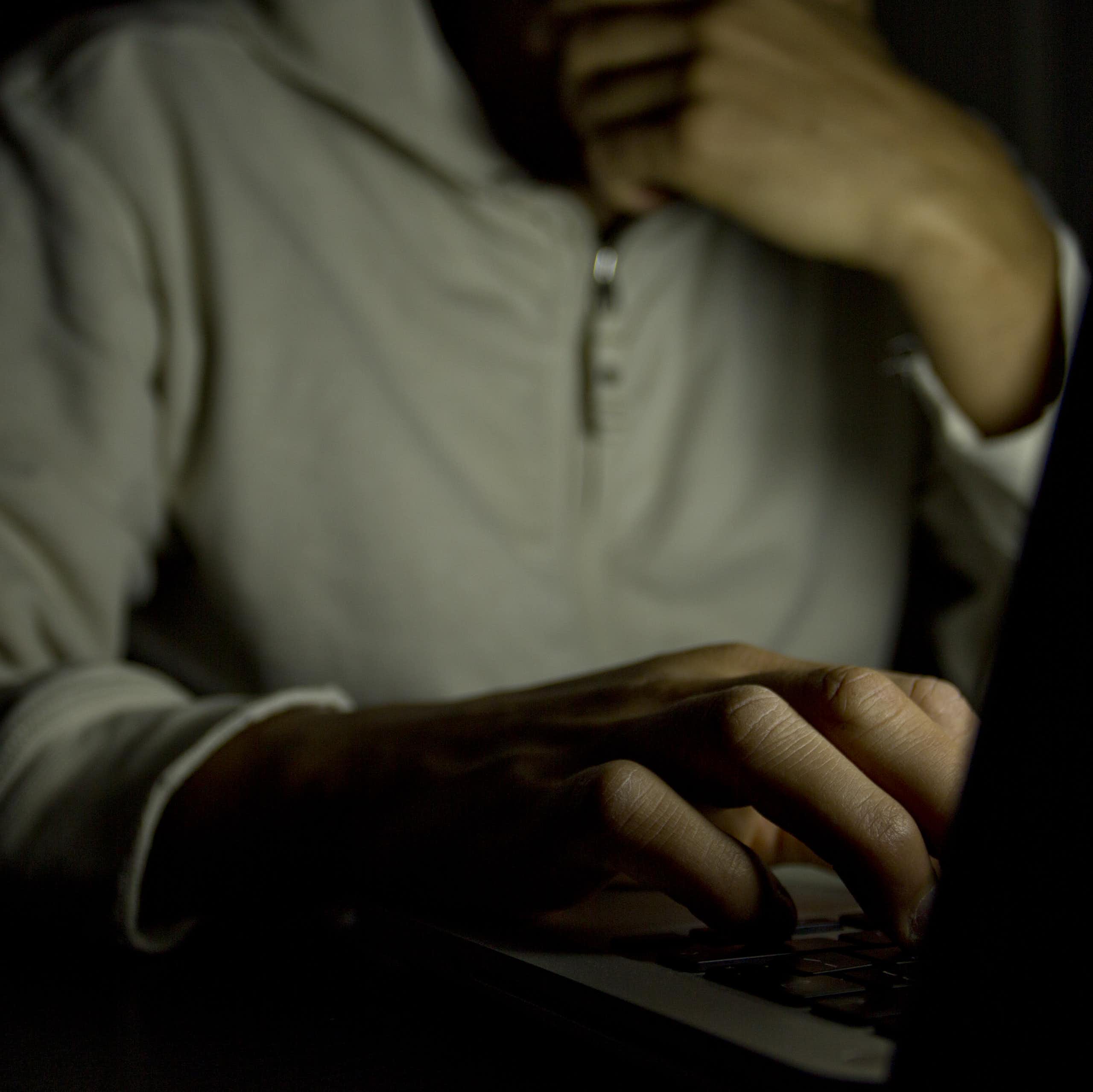 Anonymous man in shadow typing on a laptop