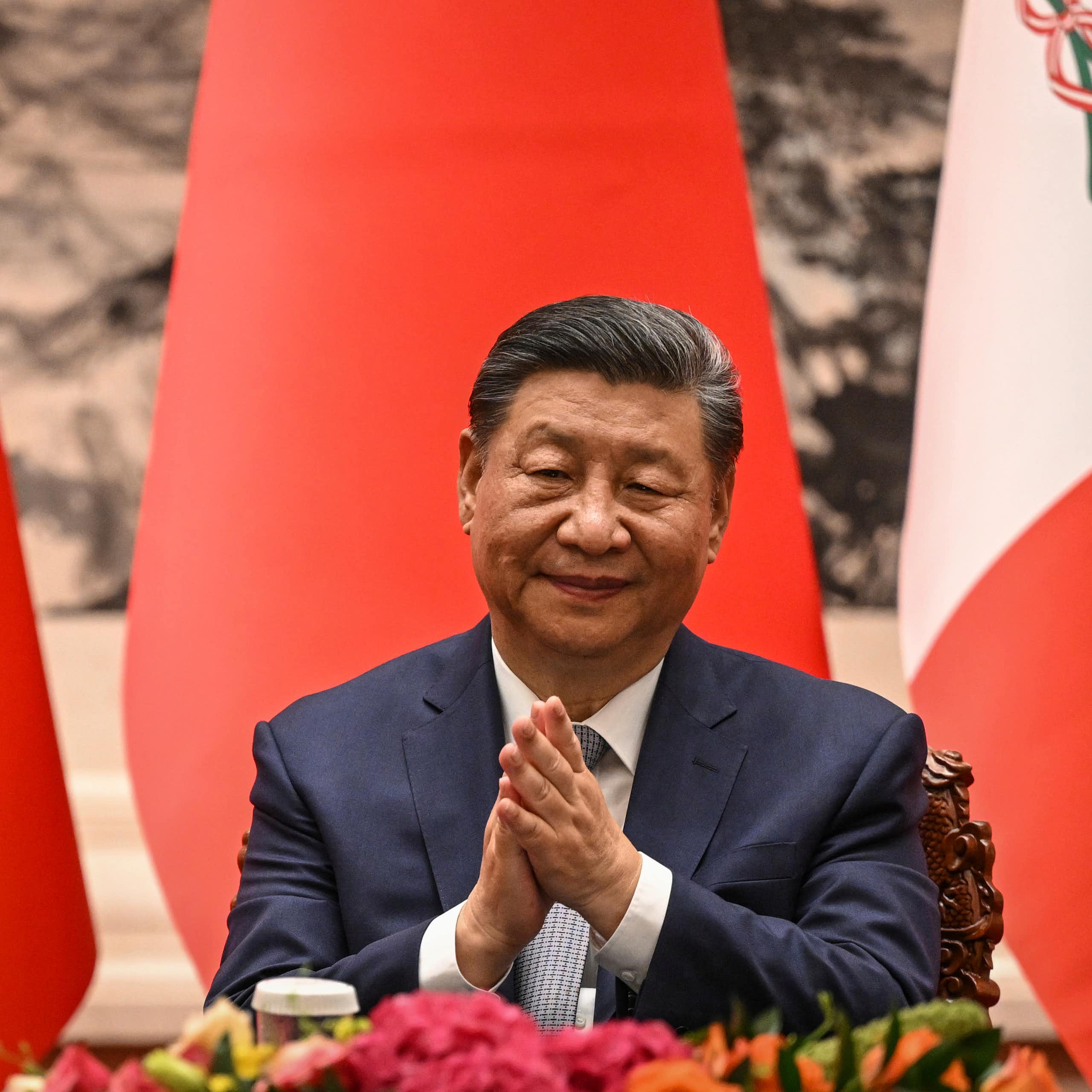 A man sitting in front of flags claps his hands