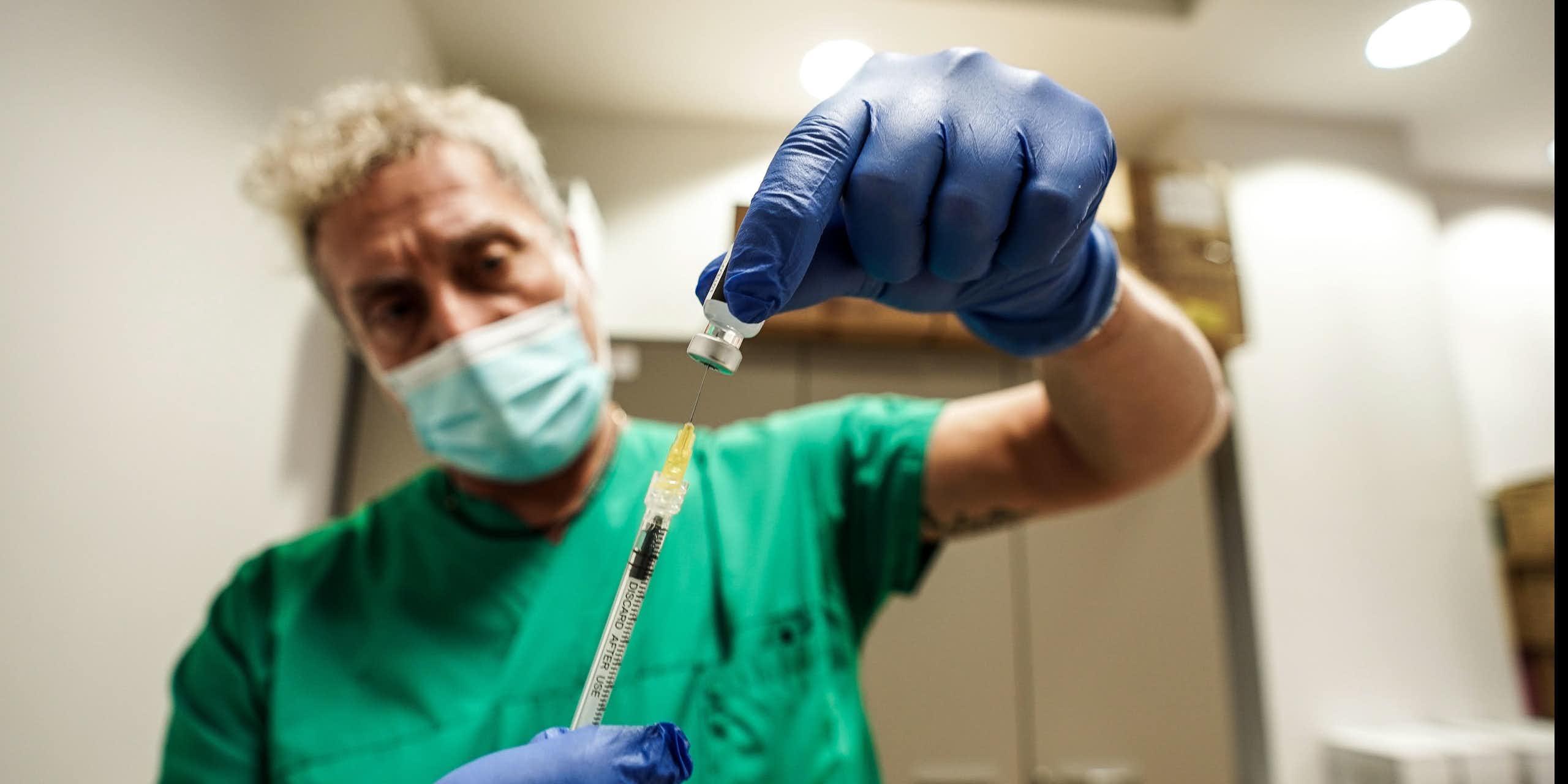 A man in green scrubs drawing up a vaccine.