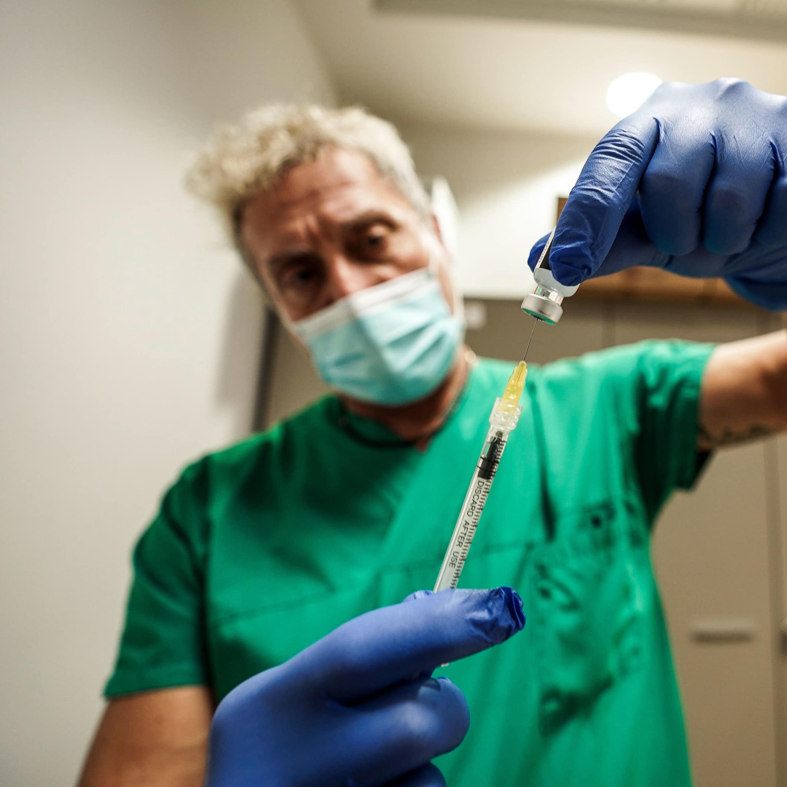 A man in green scrubs drawing up a vaccine.