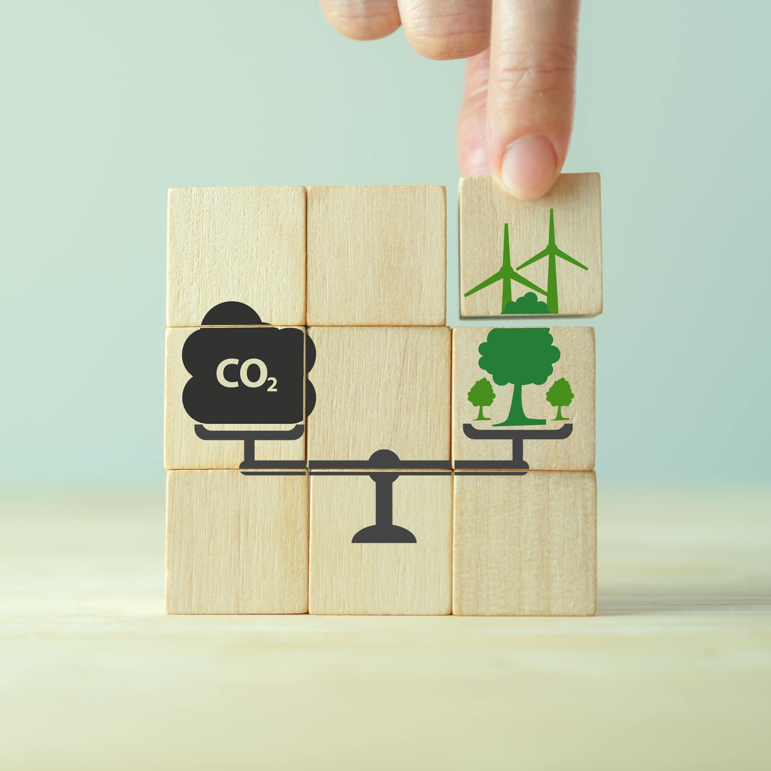 Des blocs représentent une balance pesant des émissions de CO₂ et des compensations carbone