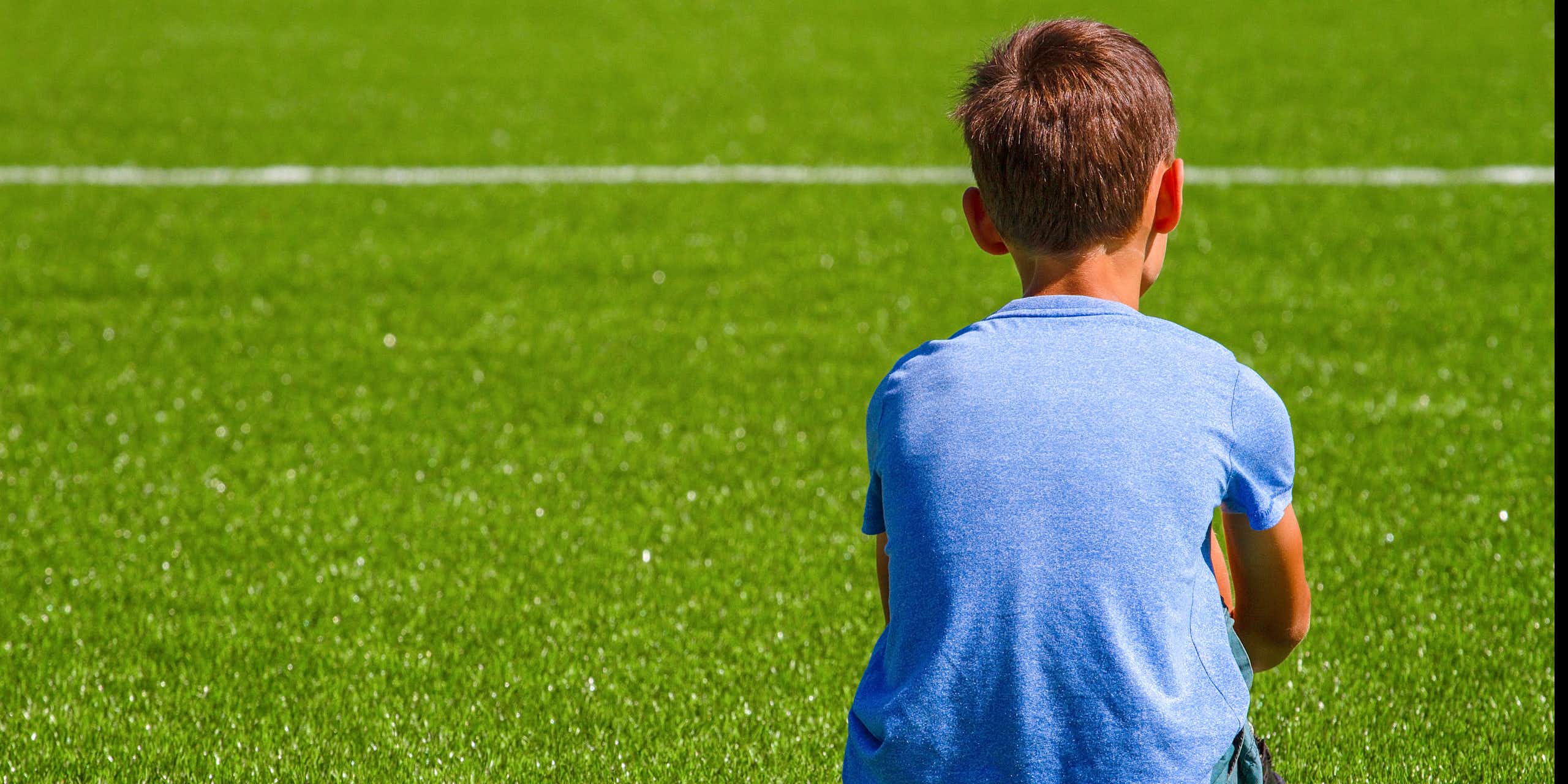 Jeune garçon de dos, assis sur un terrain de sport