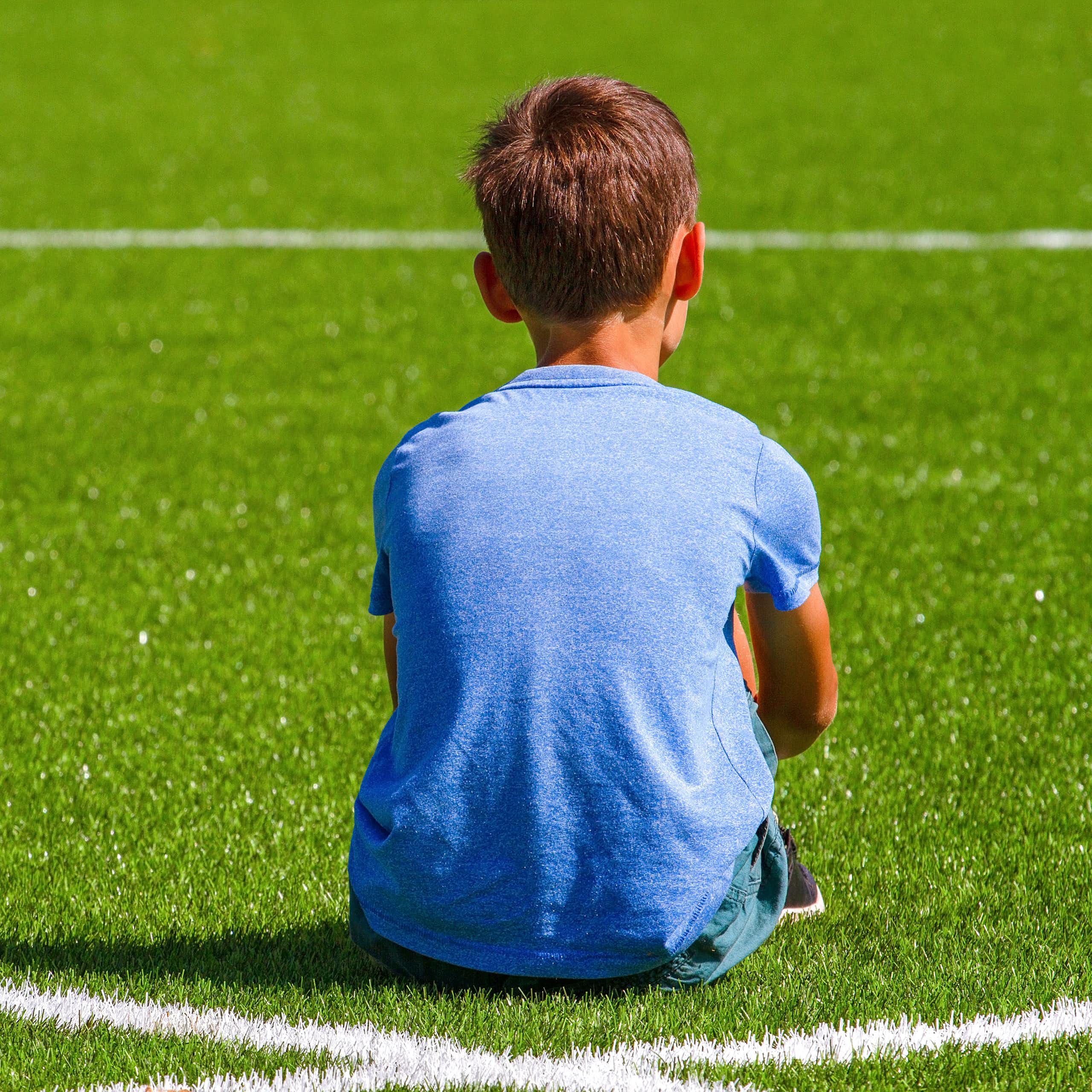 Jeune garçon de dos, assis sur un terrain de sport