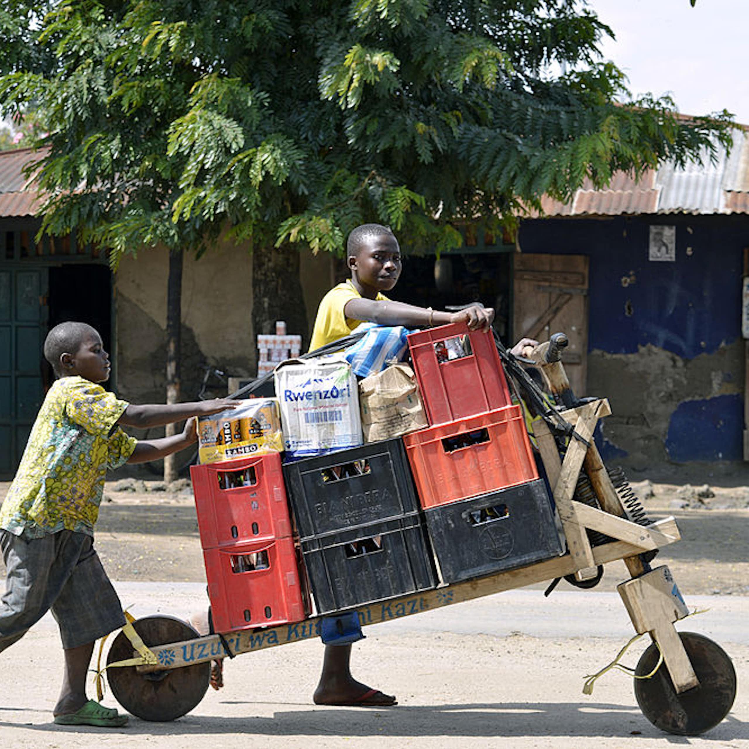 Congolese boys push a load on a two-wheeled cart through a town street.