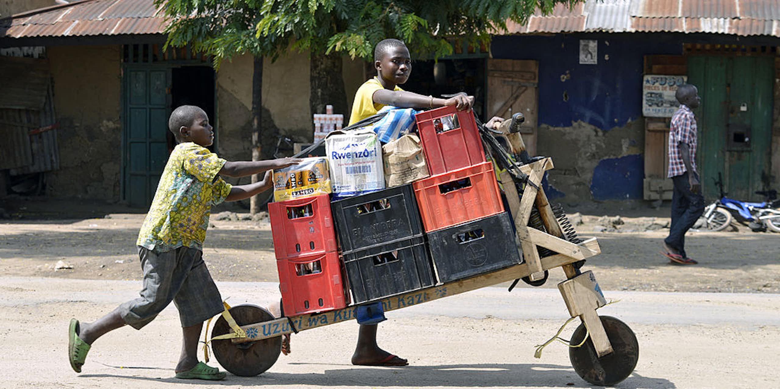 Congolese boys push a load on a two-wheeled cart through a town street.
