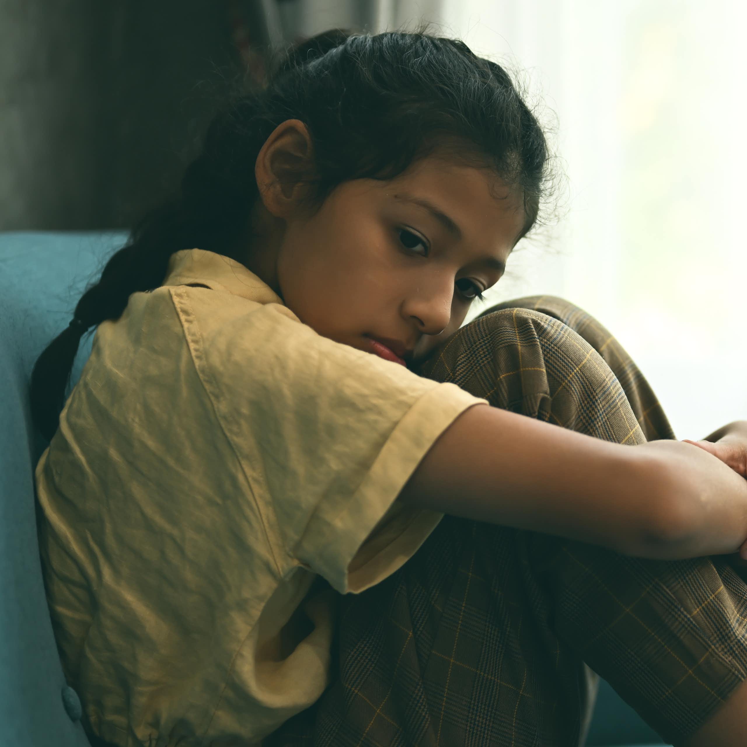 Sad girl hugs knees sitting on sofa