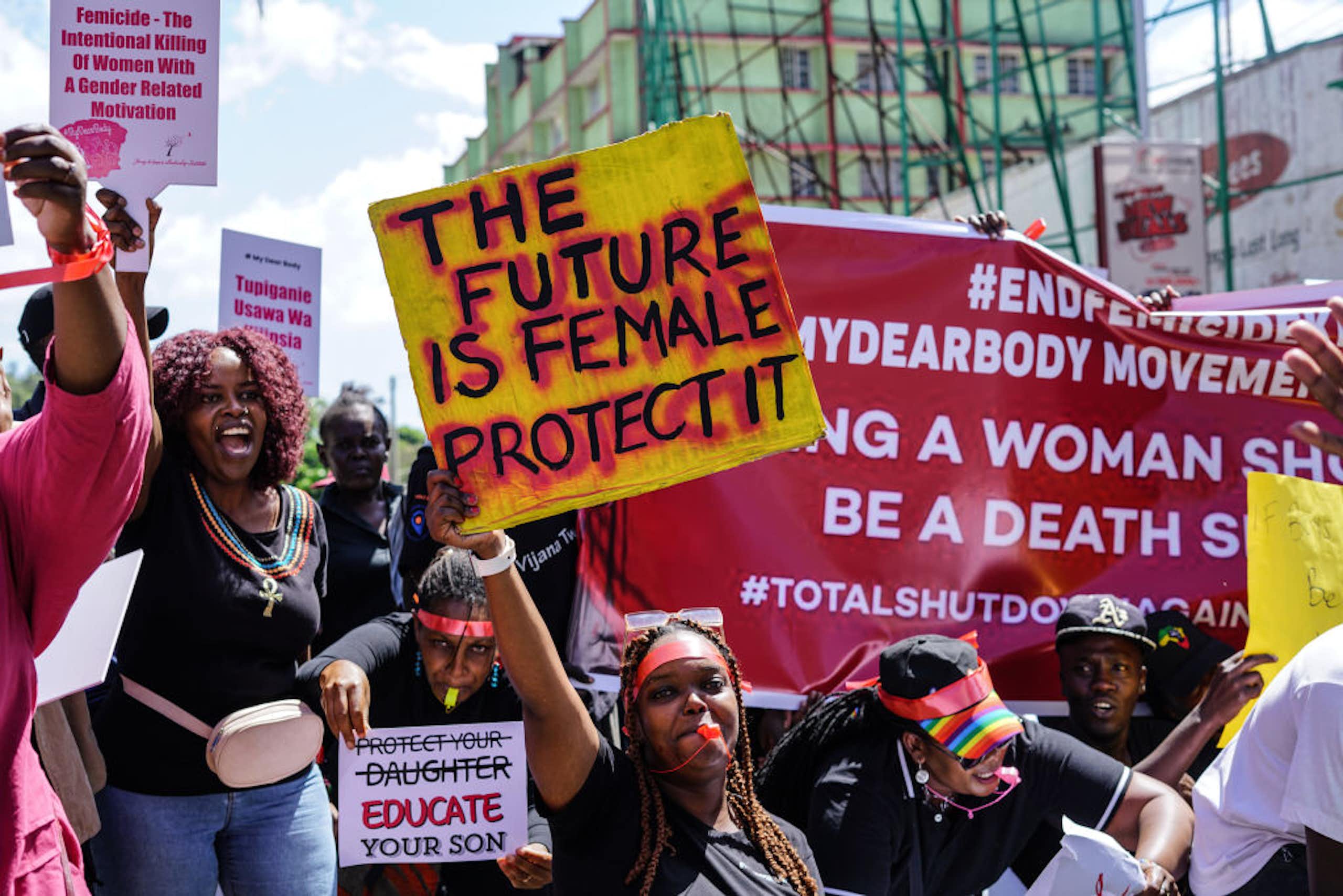 Women holding up placards and blowing into whistles with their hands up. The posters they are holding are written 'The future is female protect it' 