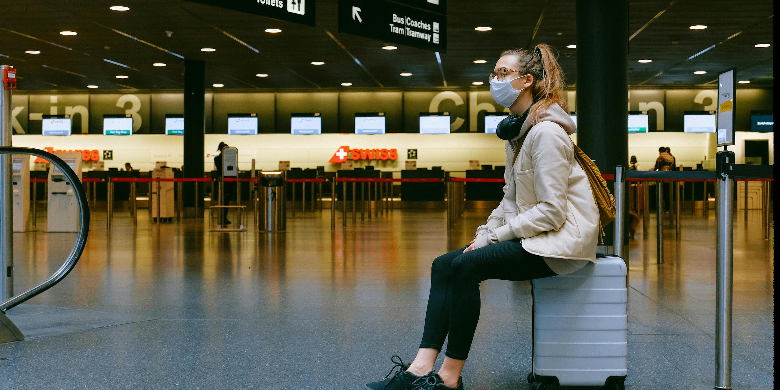 A young woman sitting on top of a suitcase in an empty airport.