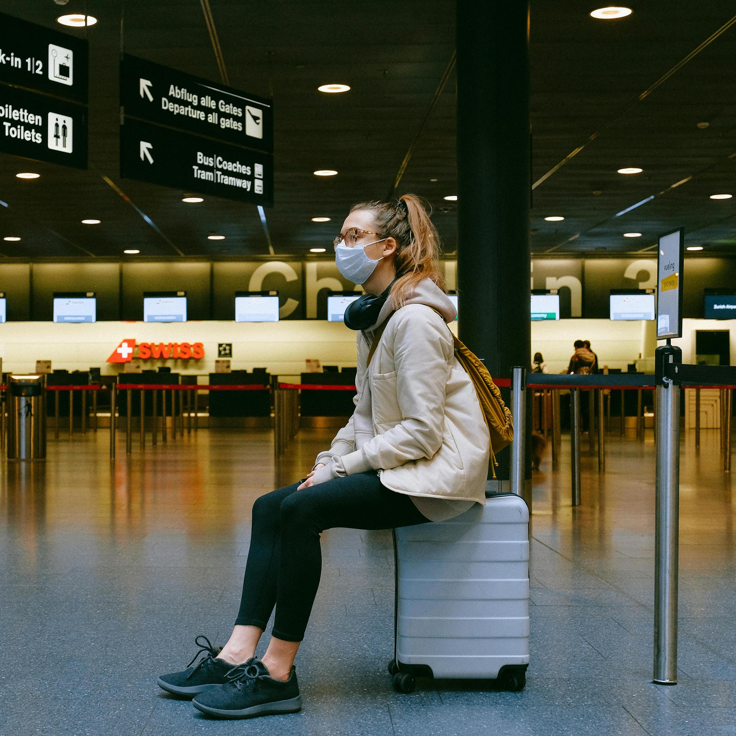A young woman sitting on top of a suitcase in an empty airport.