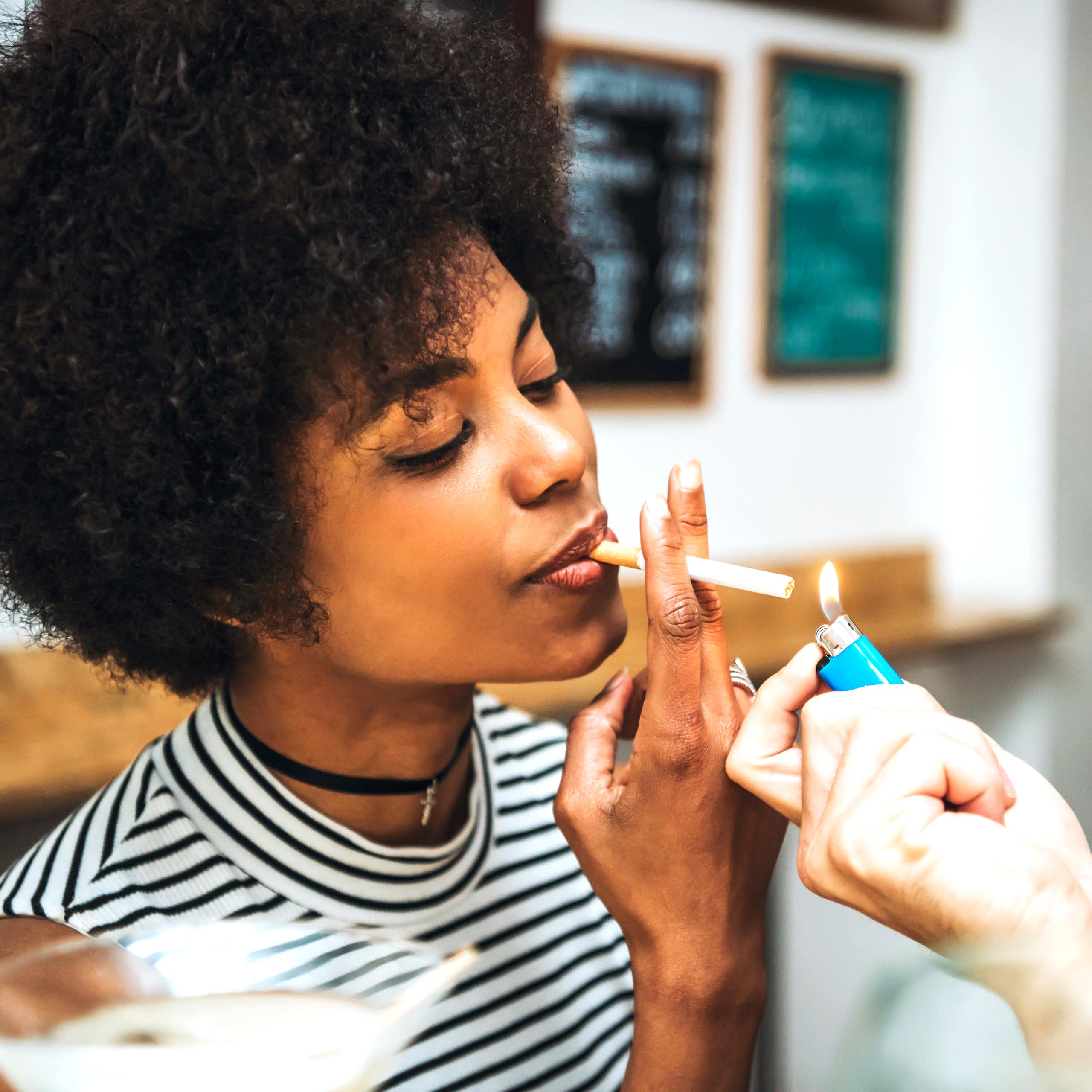A woman with a cigarette in her mouth, accepting a light from another person