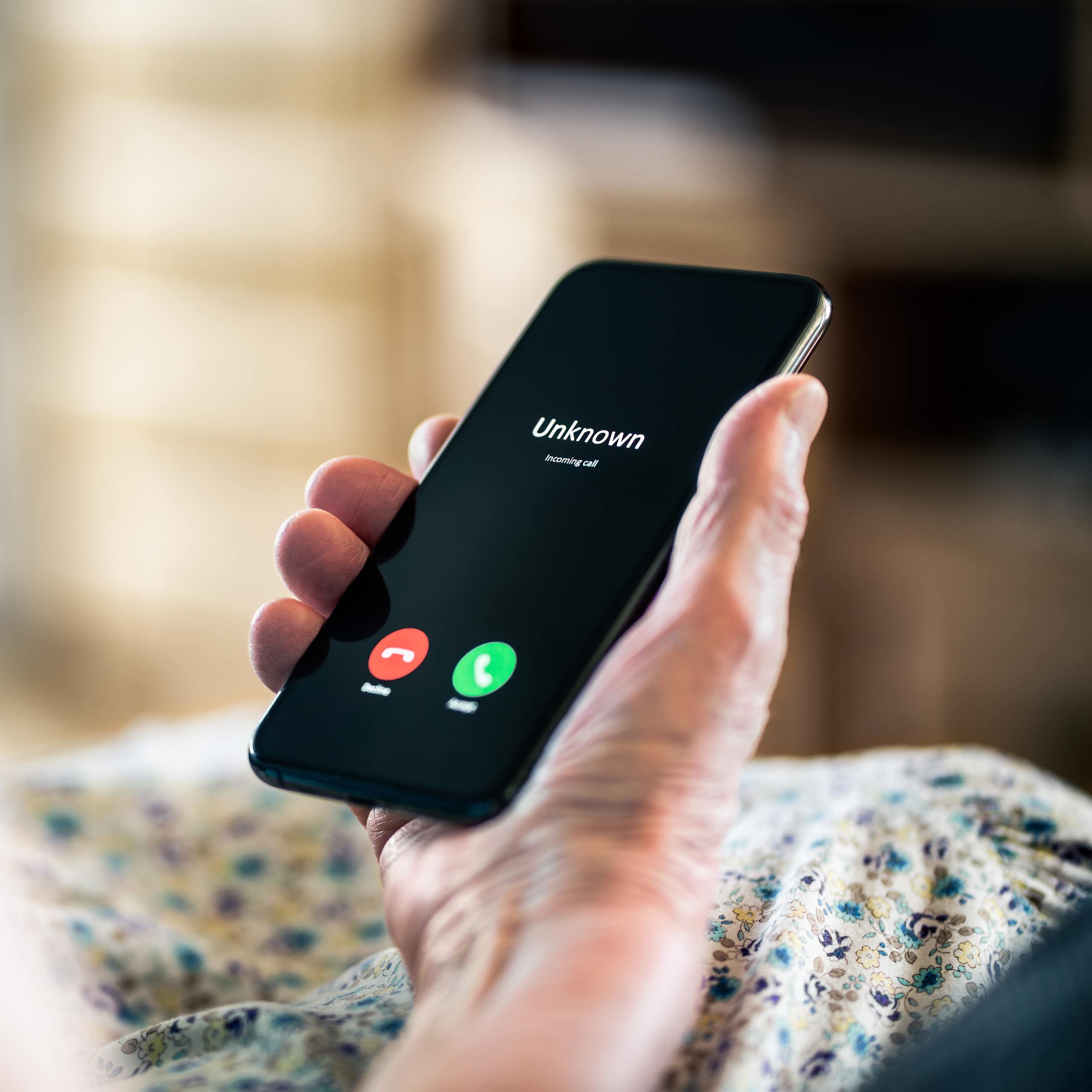 An elderly person's hand holds a cell phone.