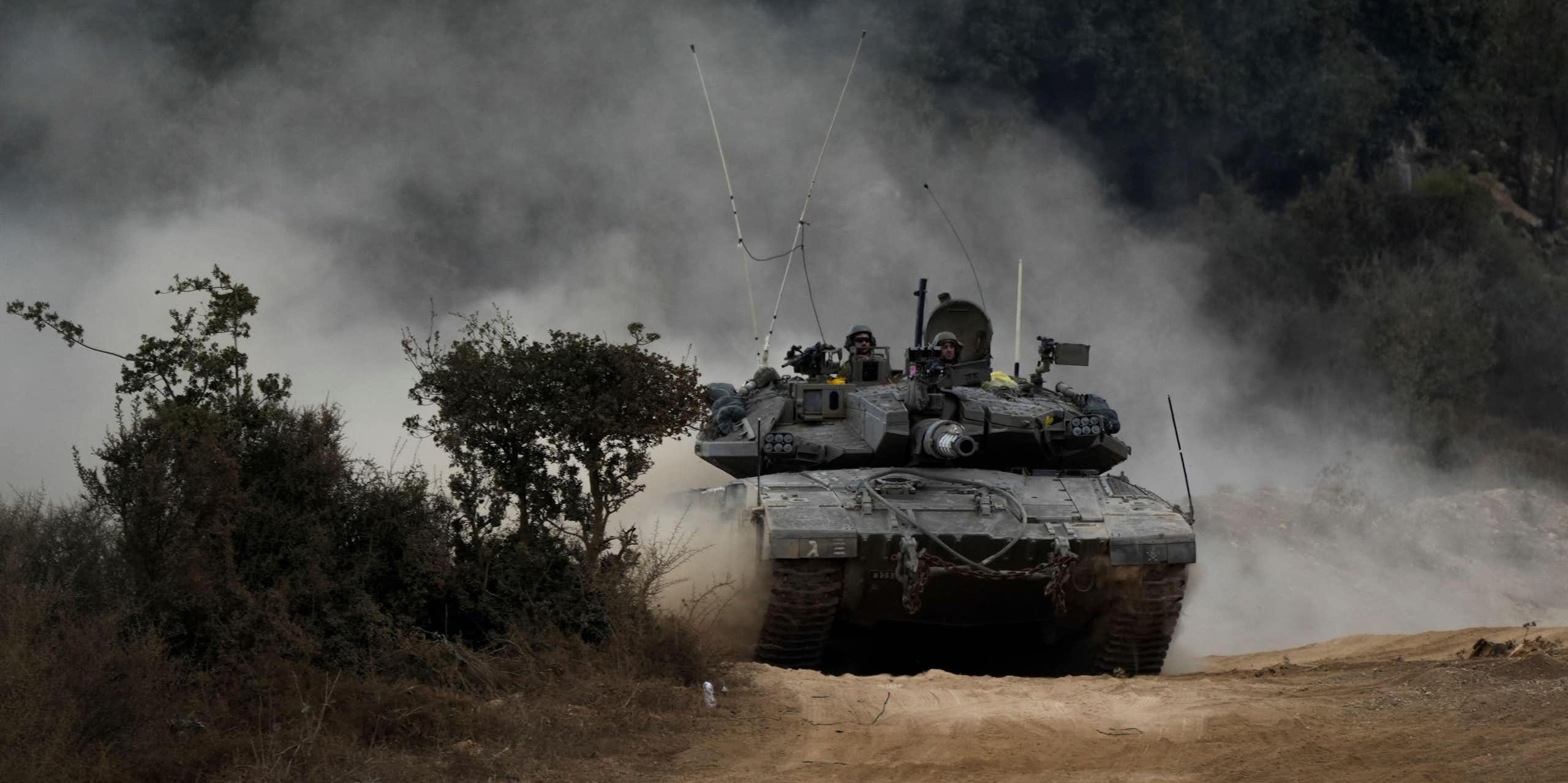 Two IDF soldiers look on as an Israeli tank manoeuvers at the Lebanese border.