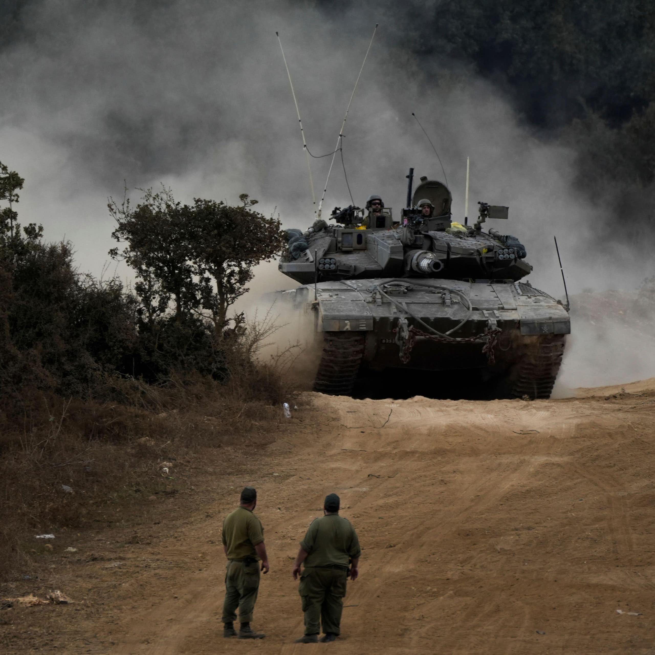 Two IDF soldiers look on as an Israeli tank manoeuvers at the Lebanese border.
