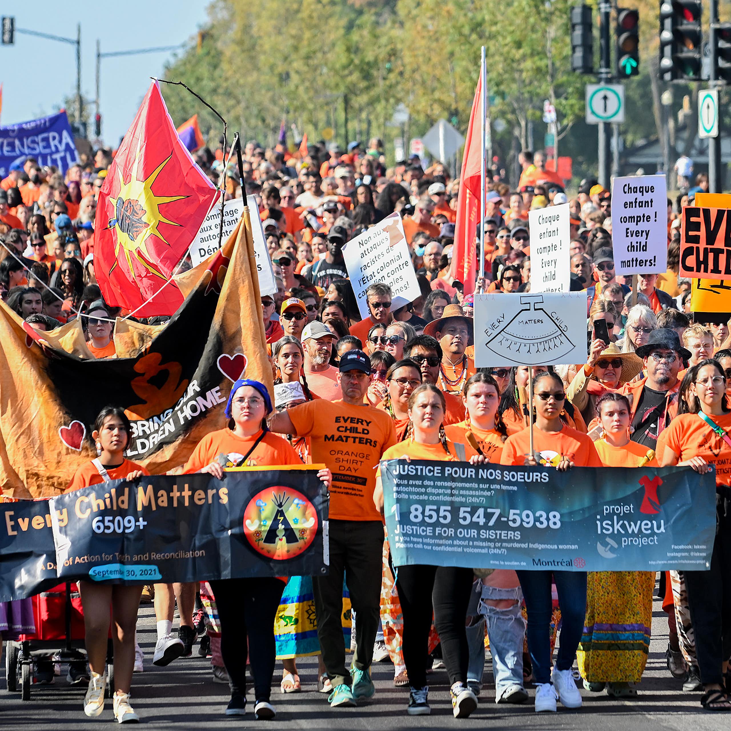 Des gens portant des chandails orange marchent en portant des affiches.