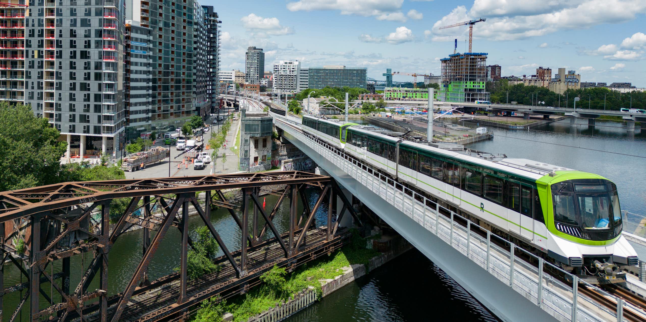 A light rail train riding a trail track over a bridge that is above a wide river