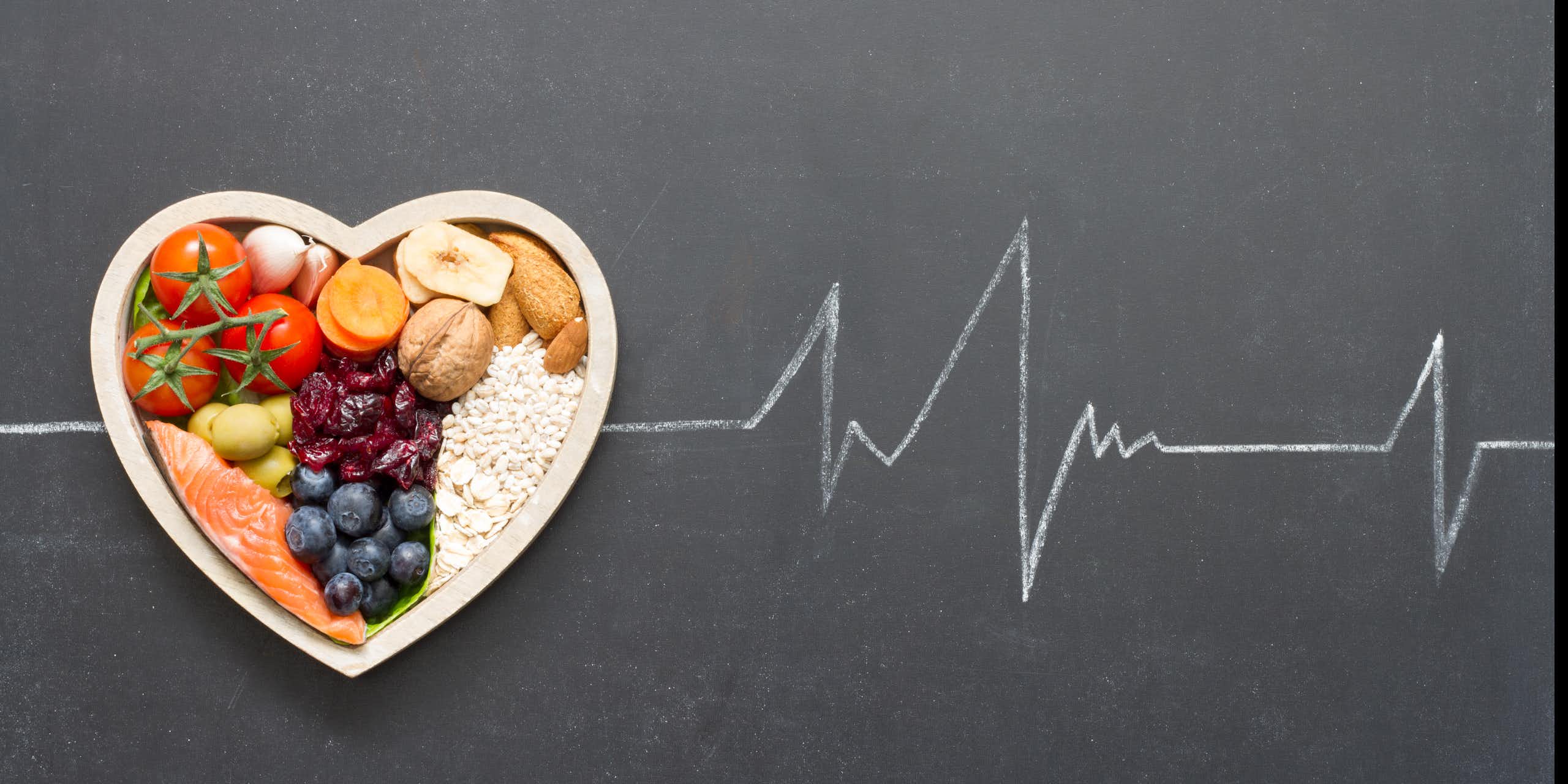 Um prato de alimentos saudáveis em forma de coração contra um quadro negro com um contorno de giz de uma leitura de eletrocardiograma