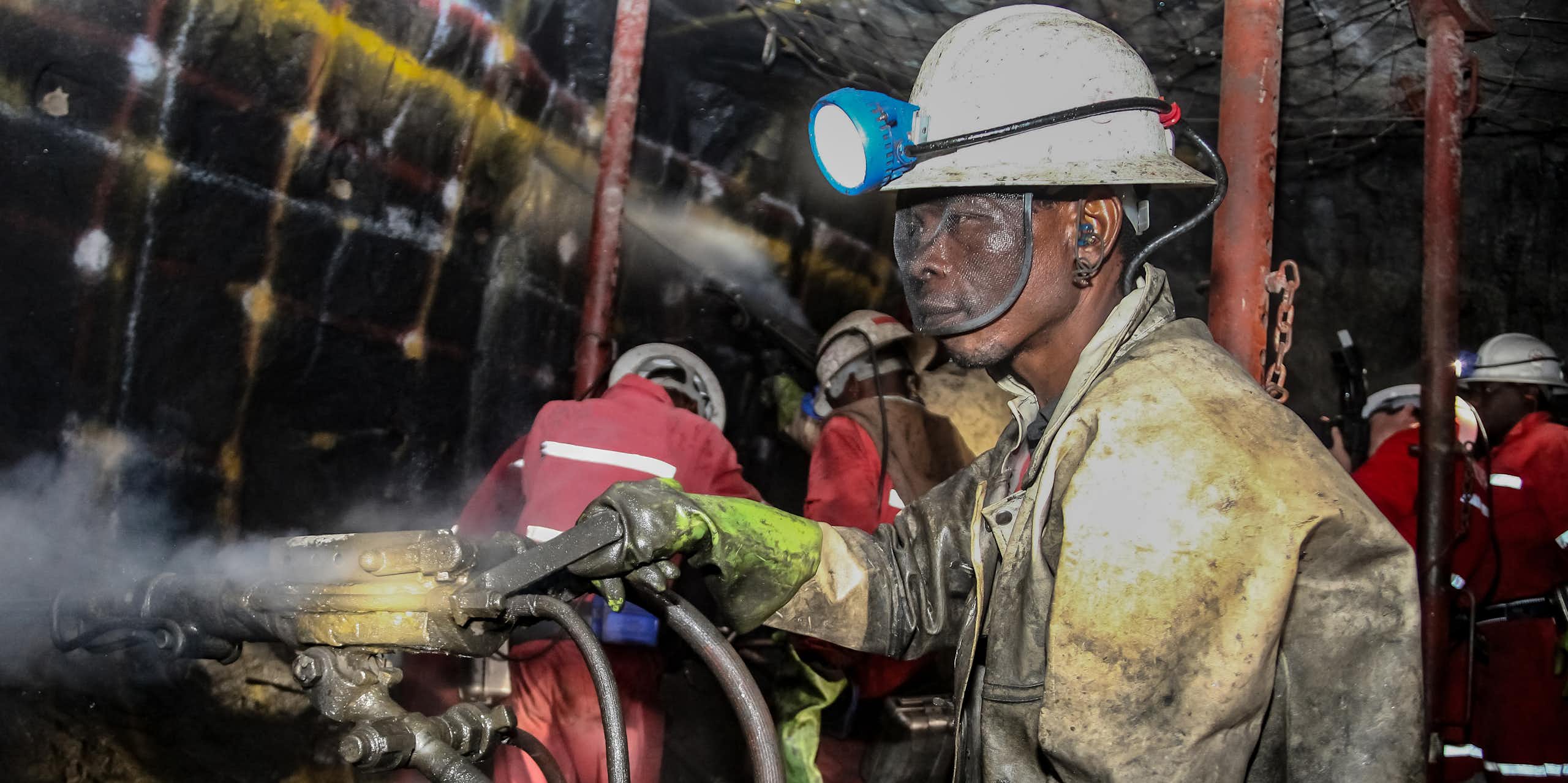 A man in a hard hat and a heavy uniform, his eyes protected by safety goggles, works underground in a mine