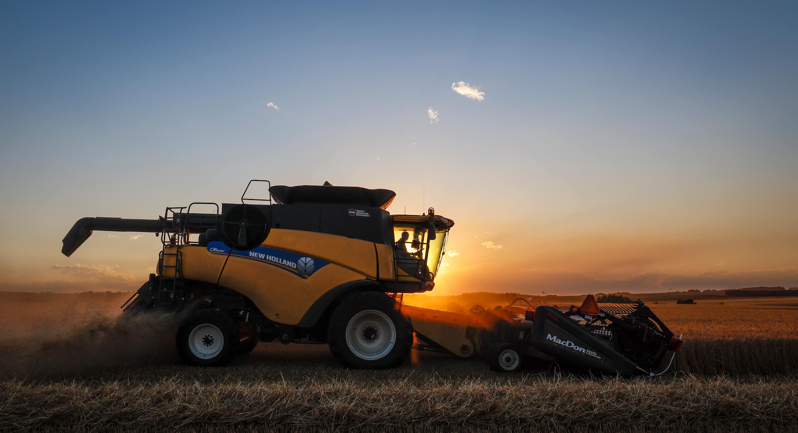 A combine harvest driving through a wheat field at sunset