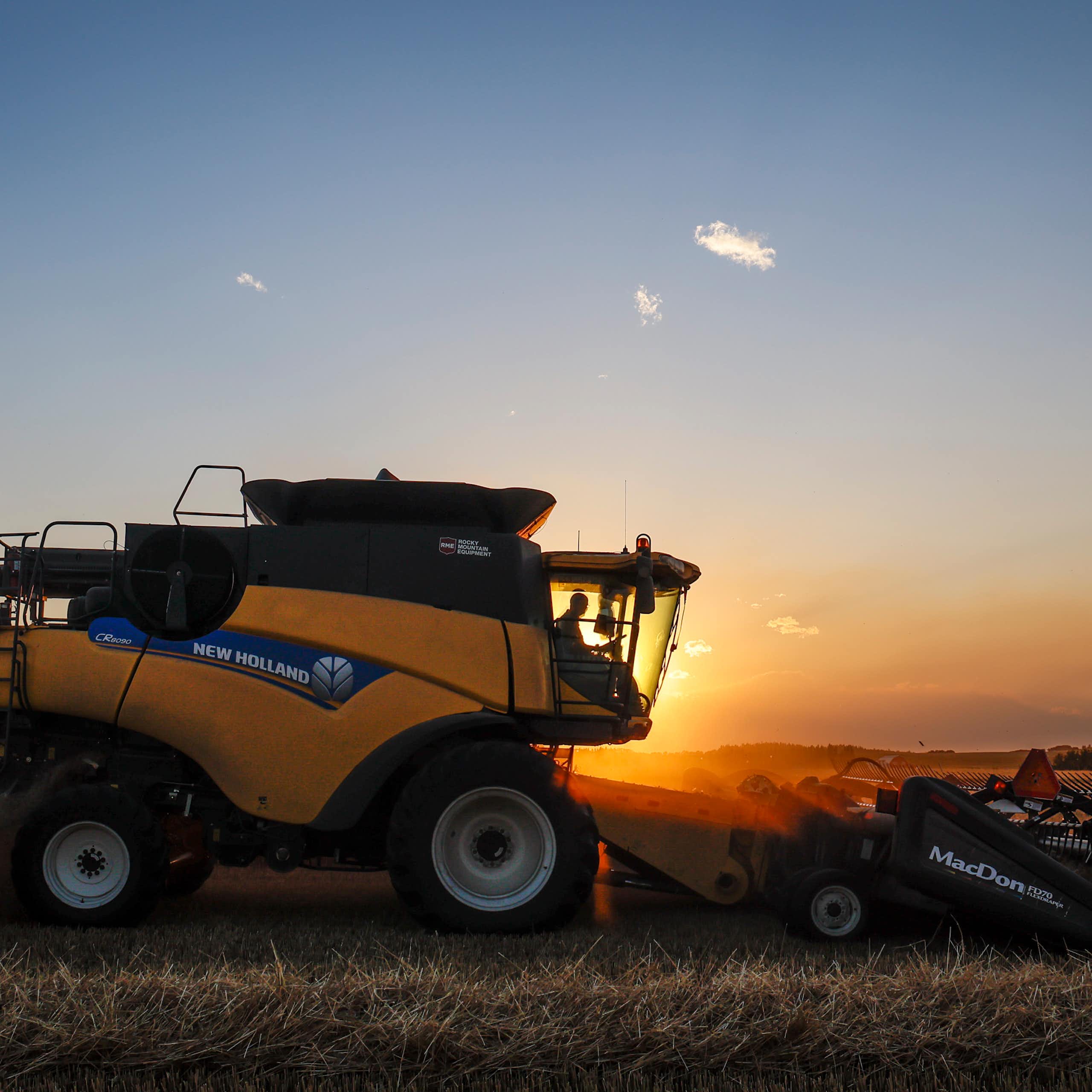 A combine harvest driving through a wheat field at sunset