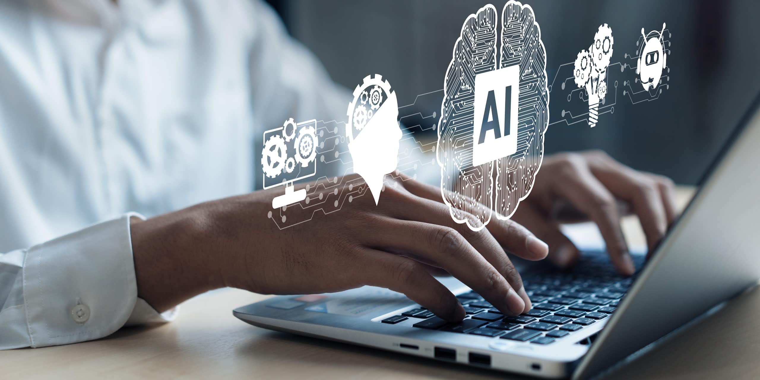 A pair of hands type on the keyboard of an open laptop with images of gear and brains float above it