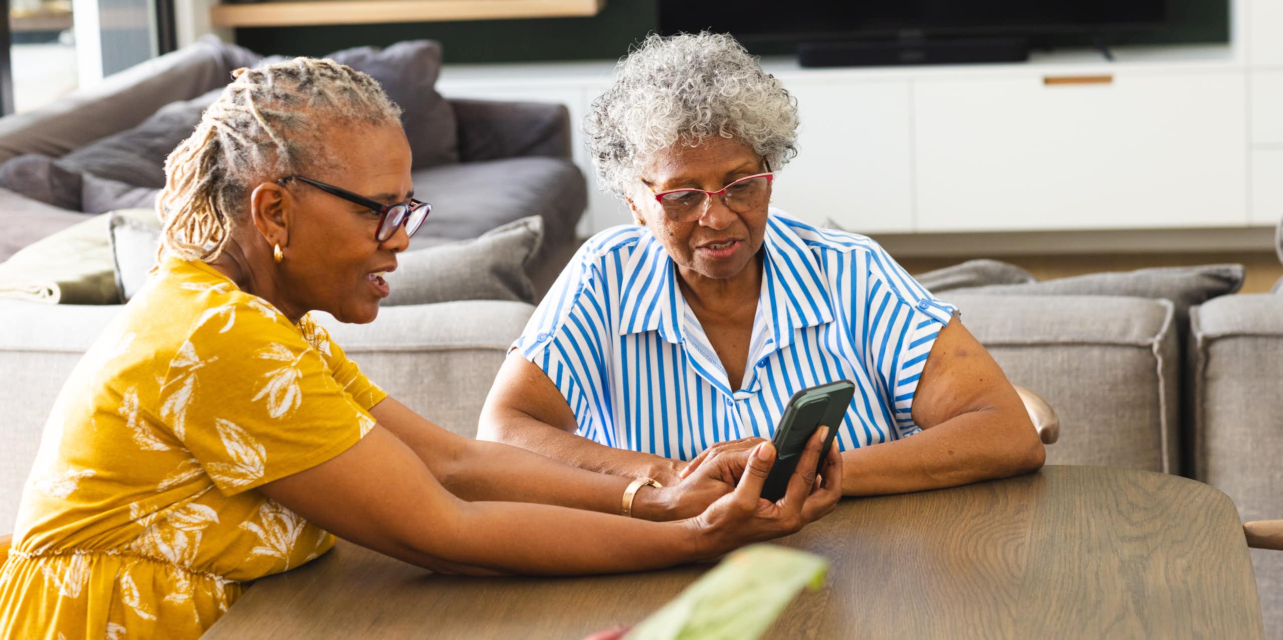 Two women sitting at a table looking at a smartphone