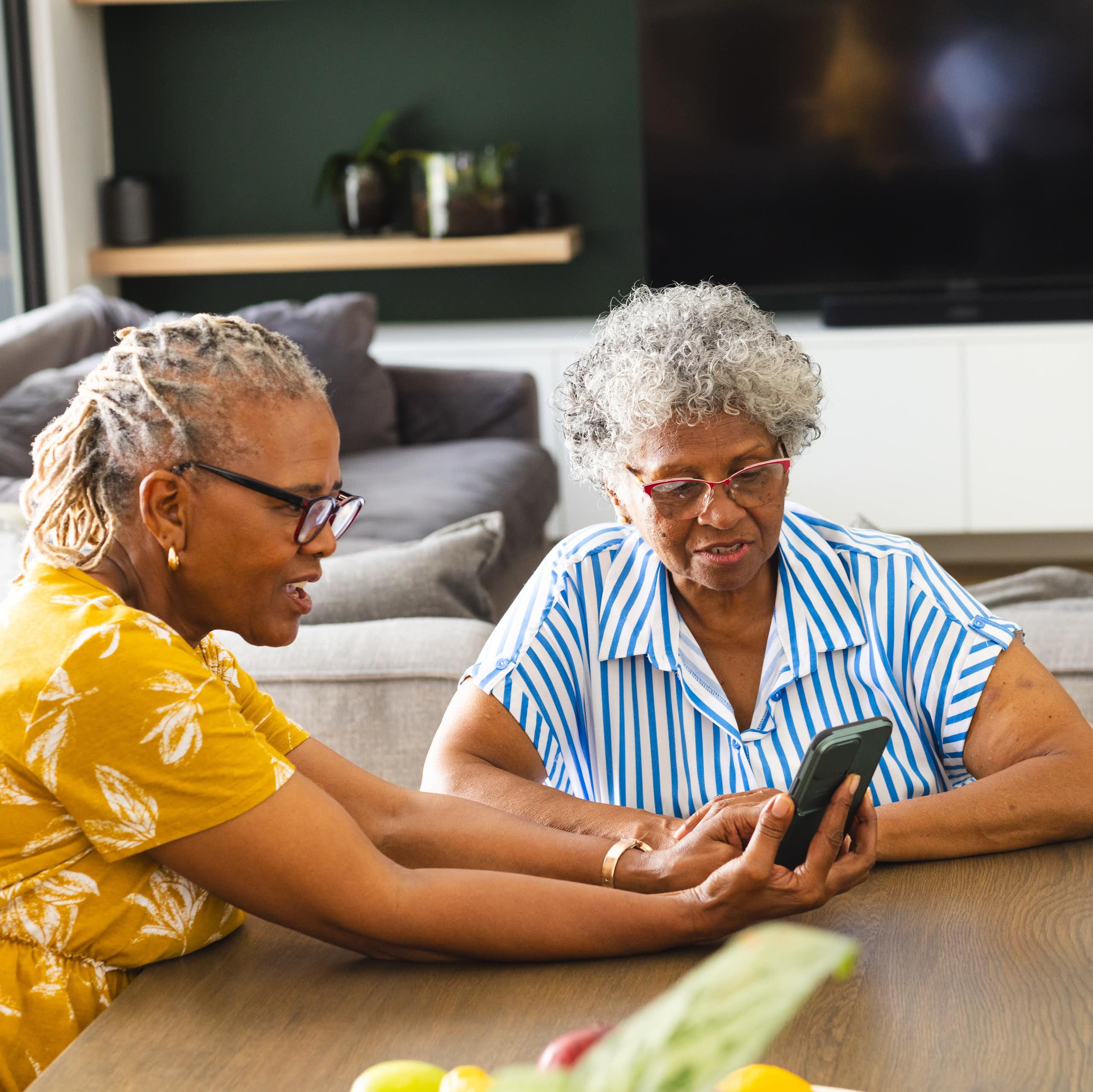Two women sitting at a table looking at a smartphone