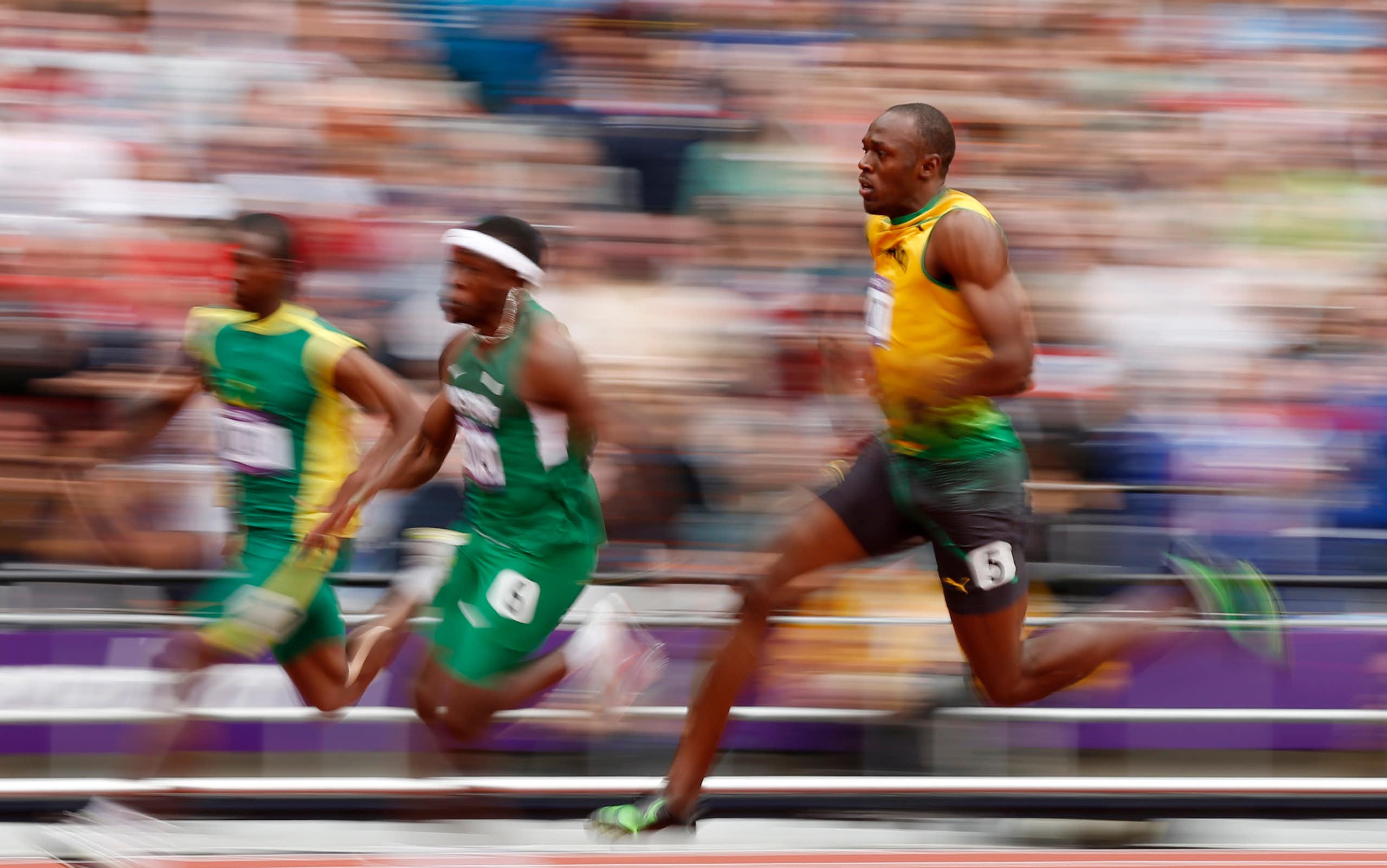 Three Olympic sprinters running on track against blurred background.