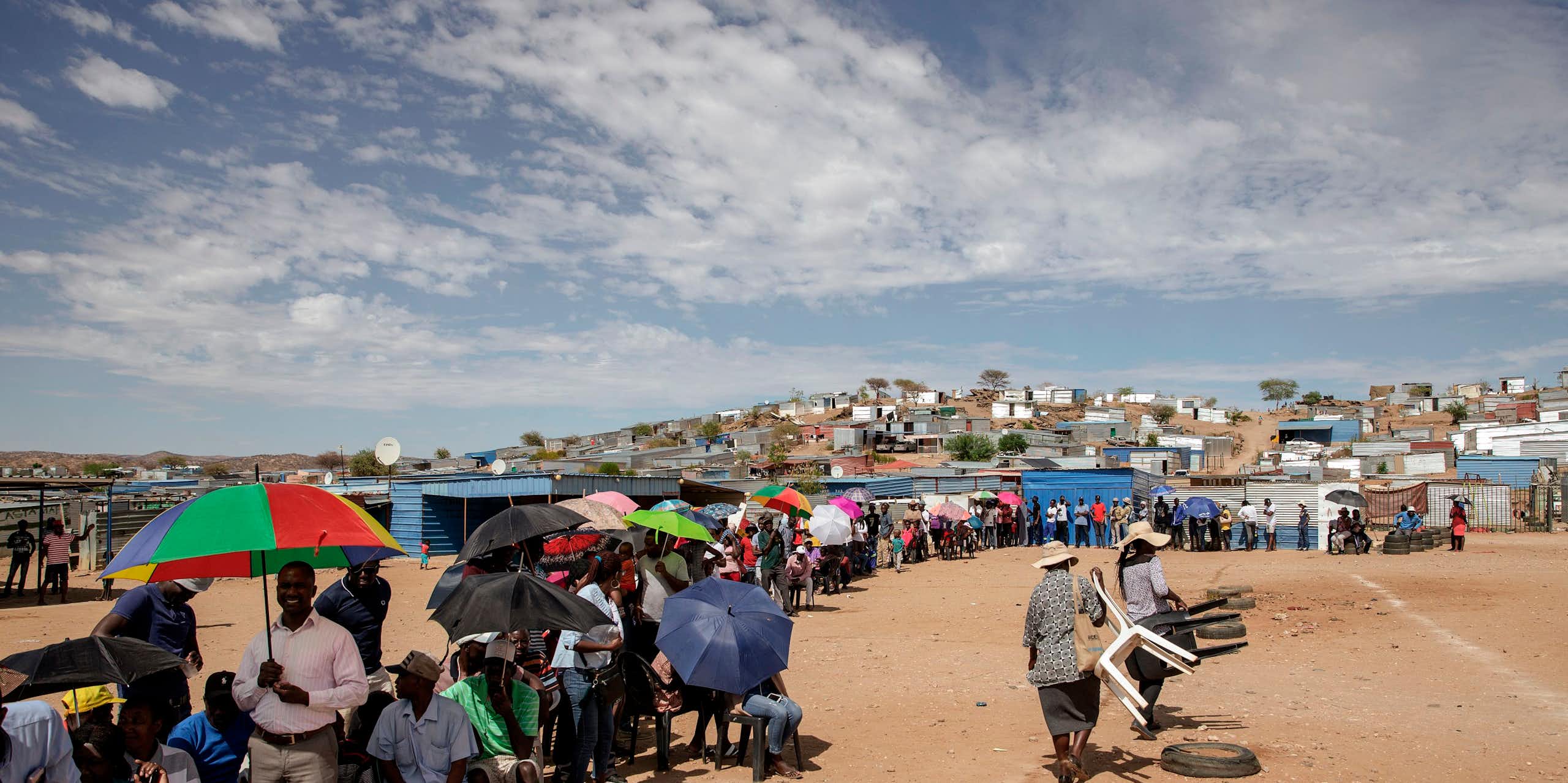 Scores of men and women, some sitting on plastic chairs, others carrying umbrellas, form a long queue outside a voting station.