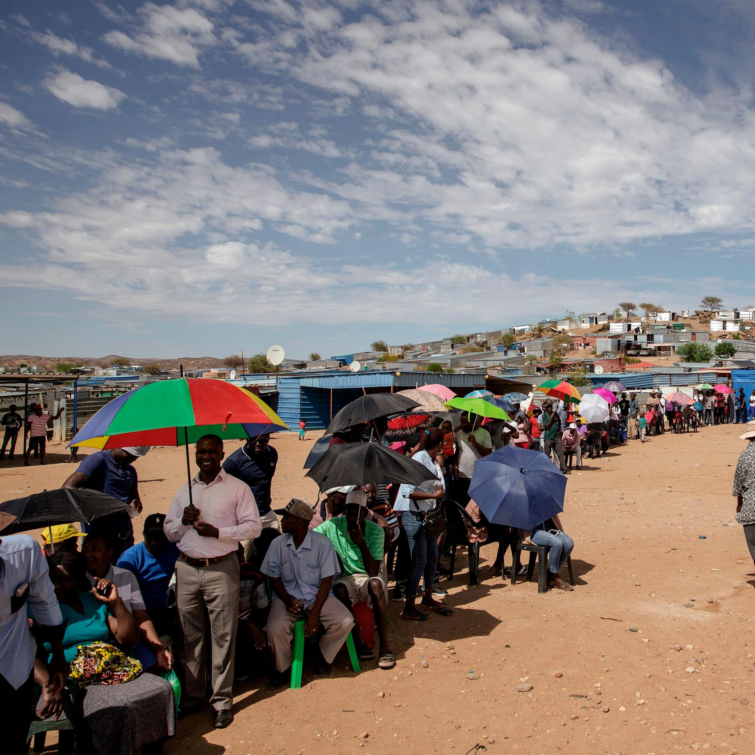 Scores of men and women, some sitting on plastic chairs, others carrying umbrellas, form a long queue outside a voting station.