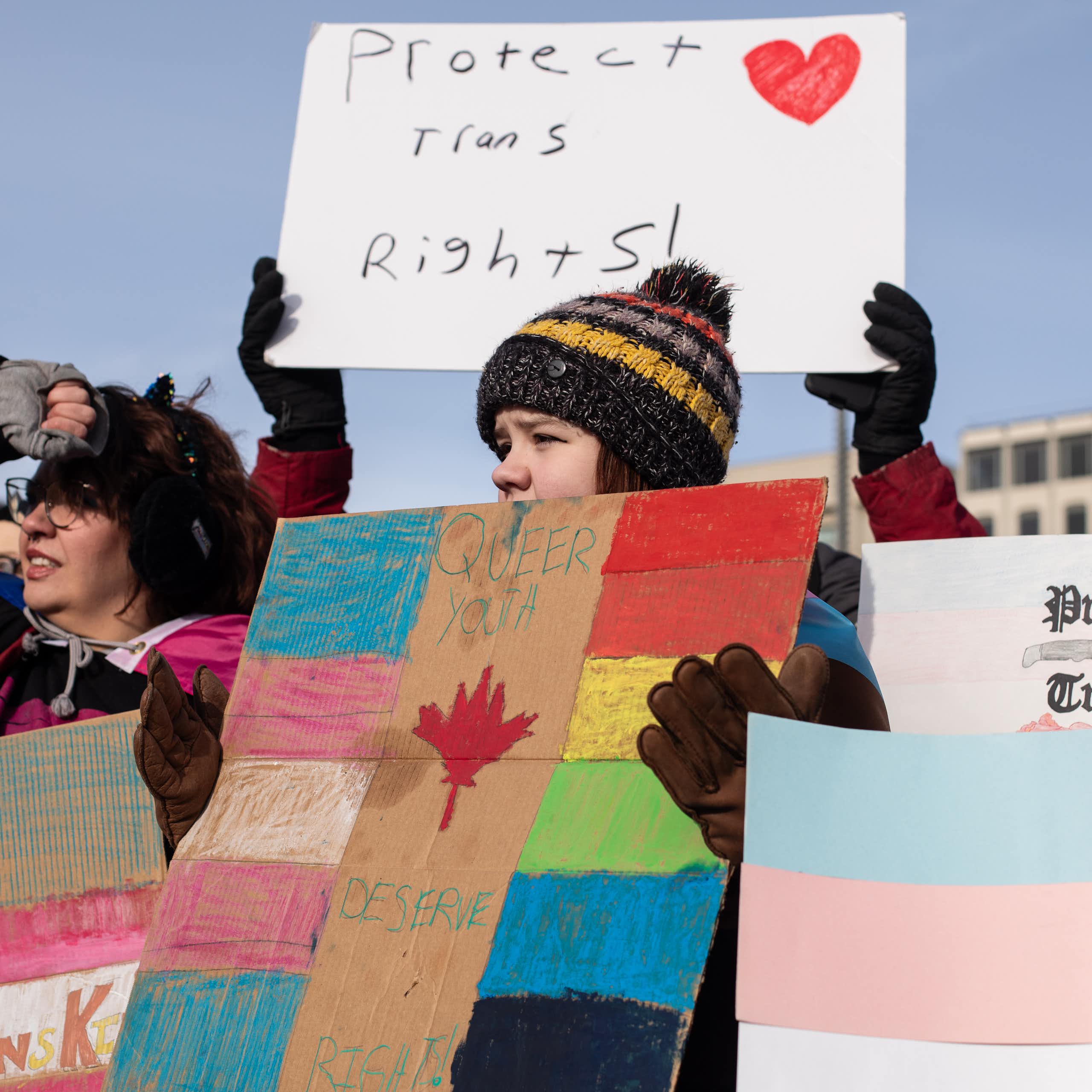 People at a protest carry signs reading: protect trans rights