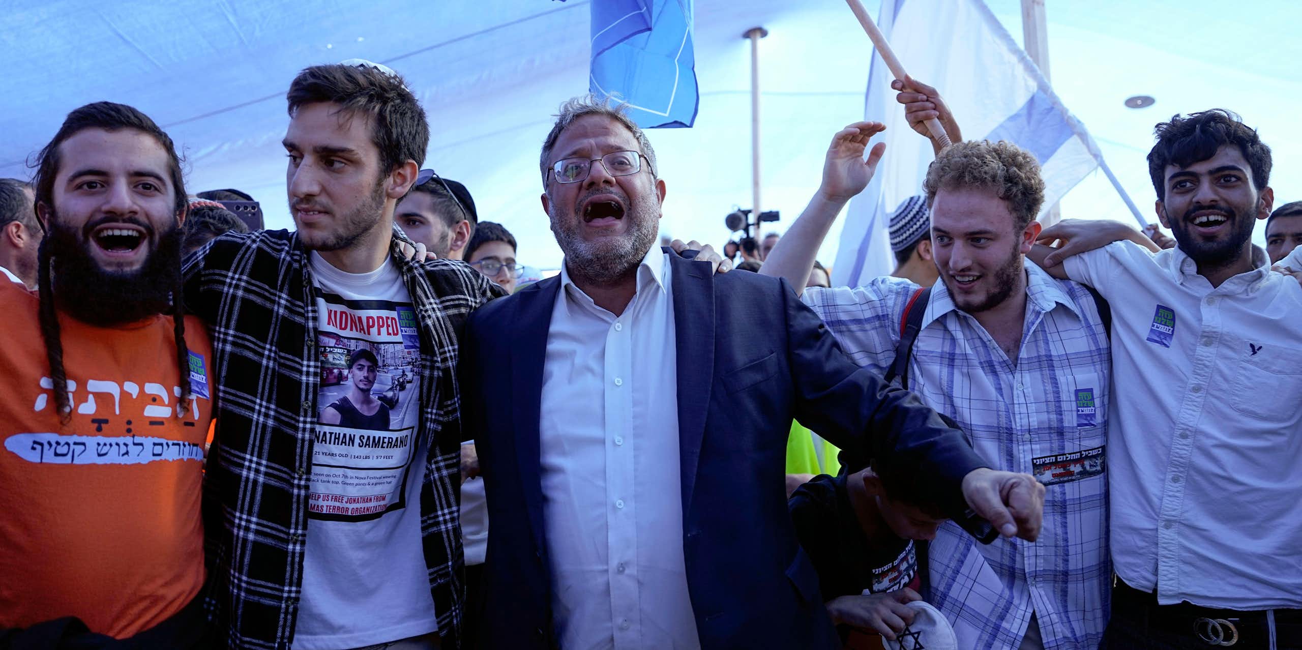 Israel's national security minister, Itamar Ben Gvir, dancing with members of the settler movement  as Israeli flags fly in the background.