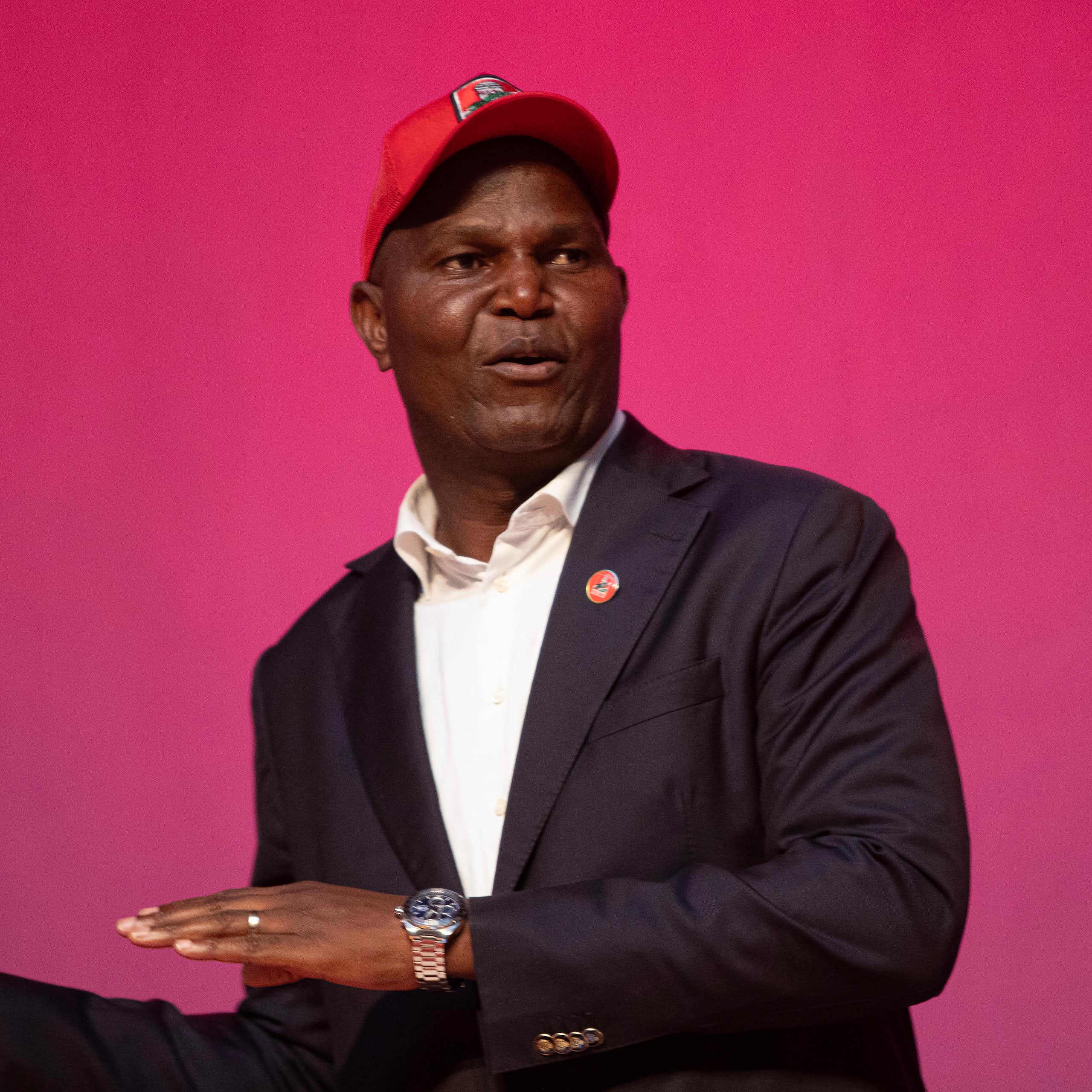  A man wearing a cap speaks to an audience.