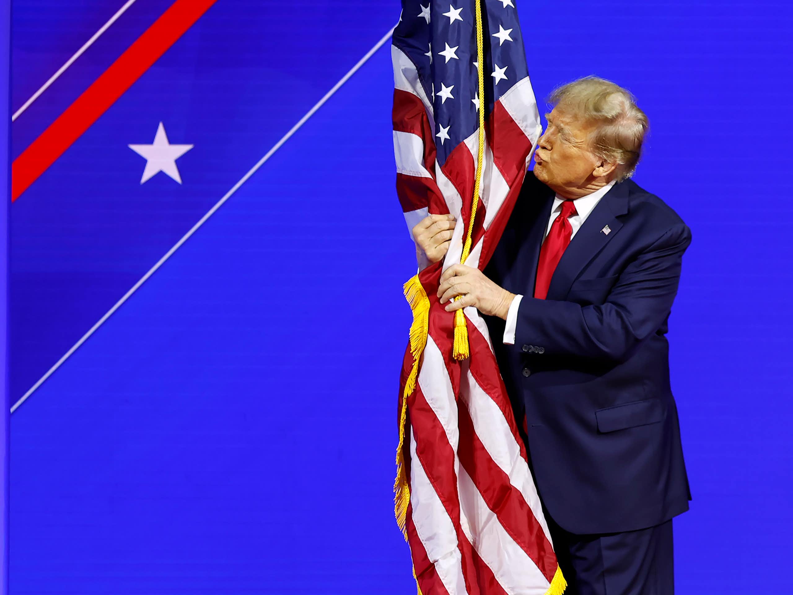 A man dressed in red, white and blue hugging and kissing an American flag.