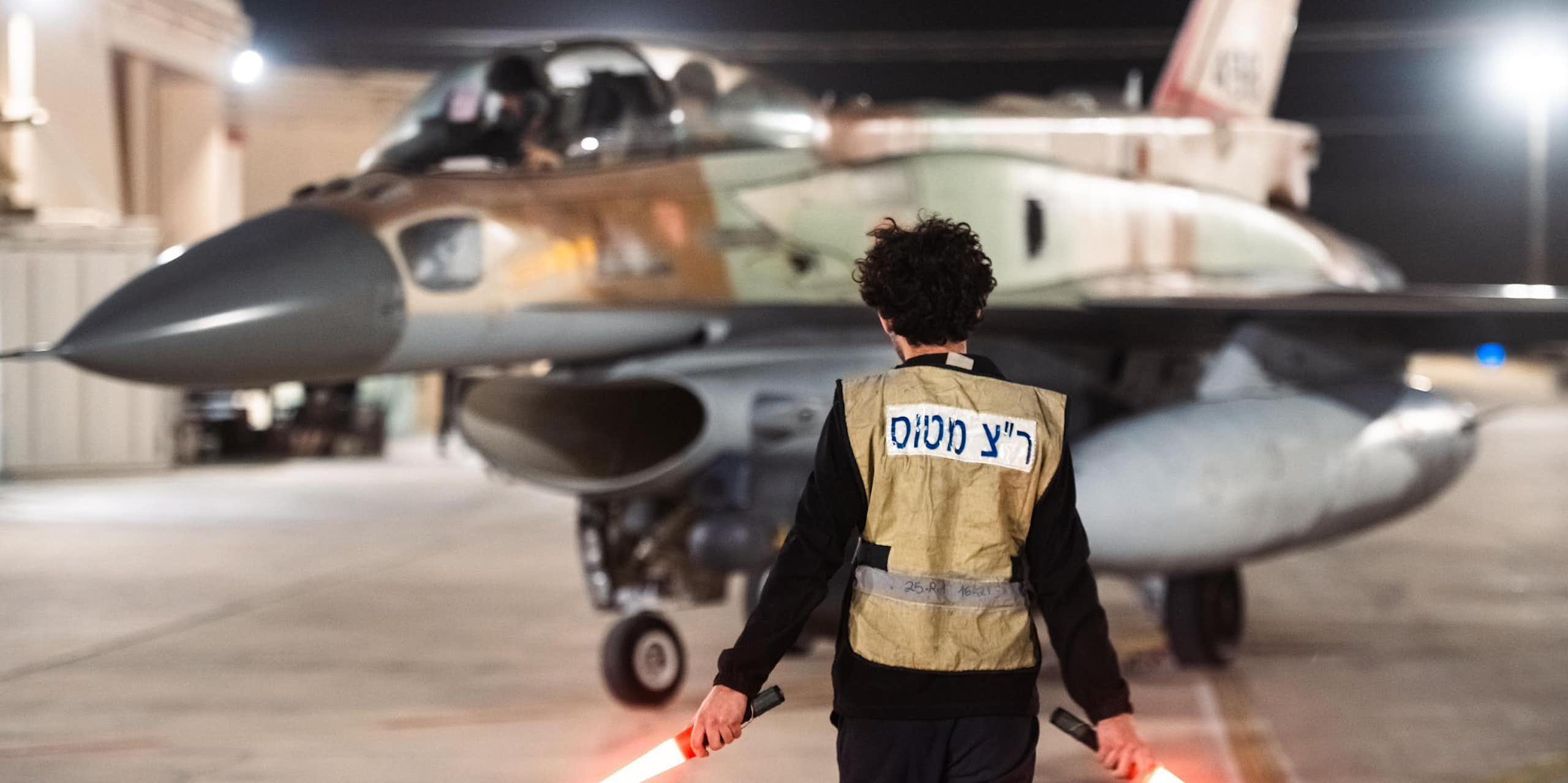A man with hand-held lights stands in front of a military jet.