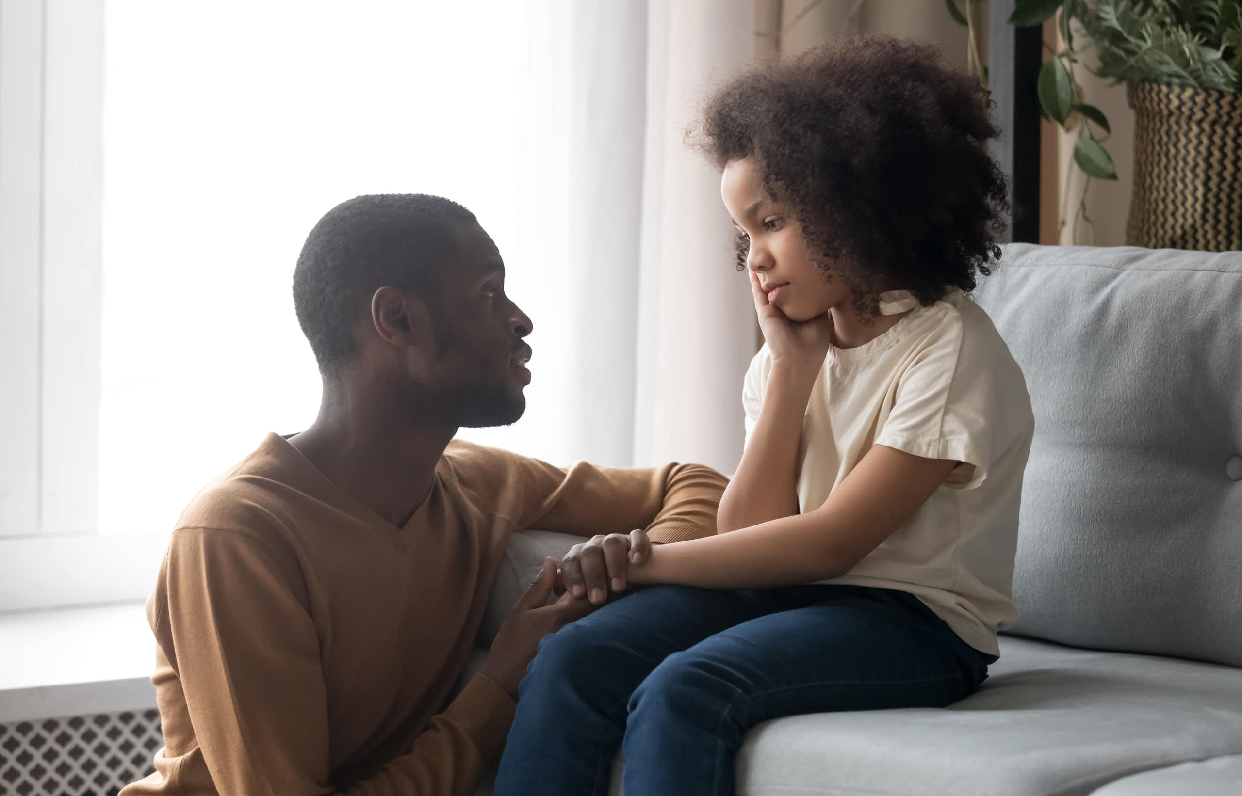 A father speaking to an upset child on a sofa