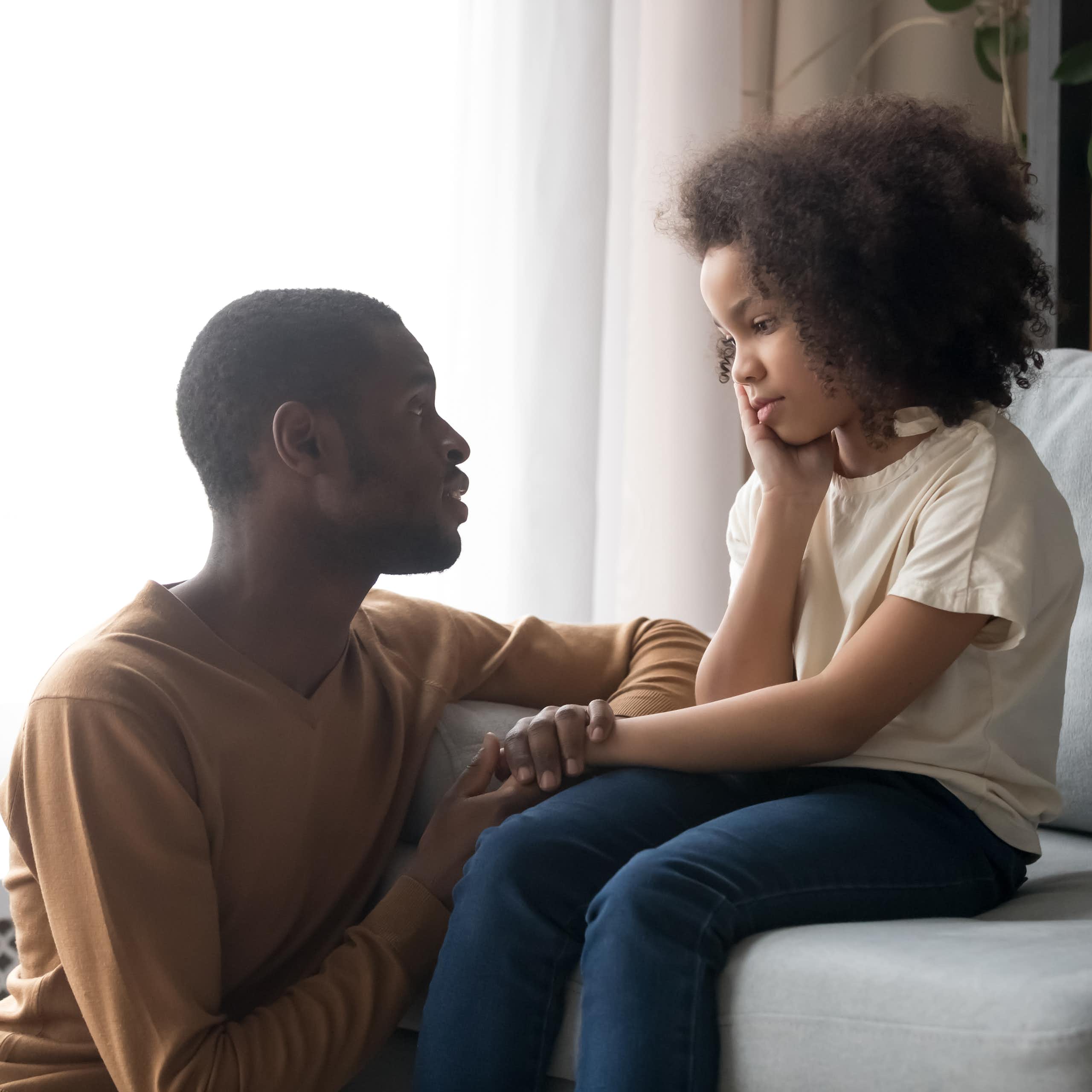 A father speaking to an upset child on a sofa