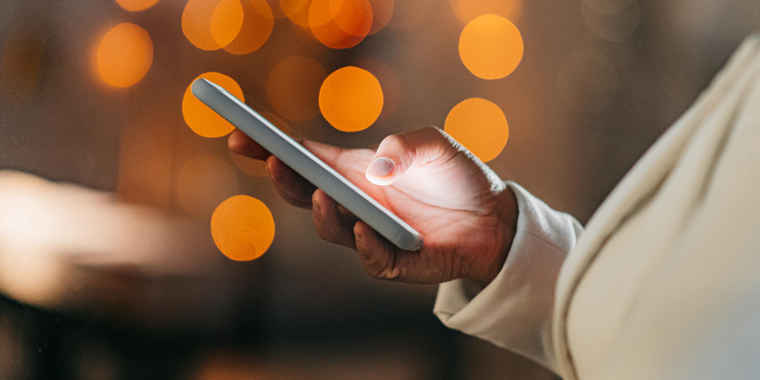 An African woman's hand holds a cell phone, orange circles of light in the background.