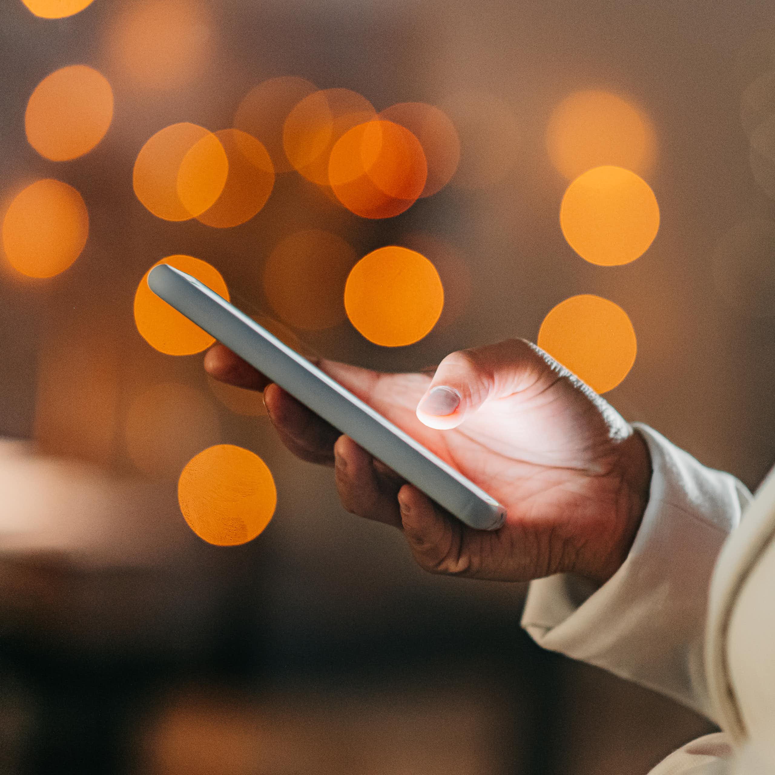An African woman's hand holds a cell phone, orange circles of light in the background.