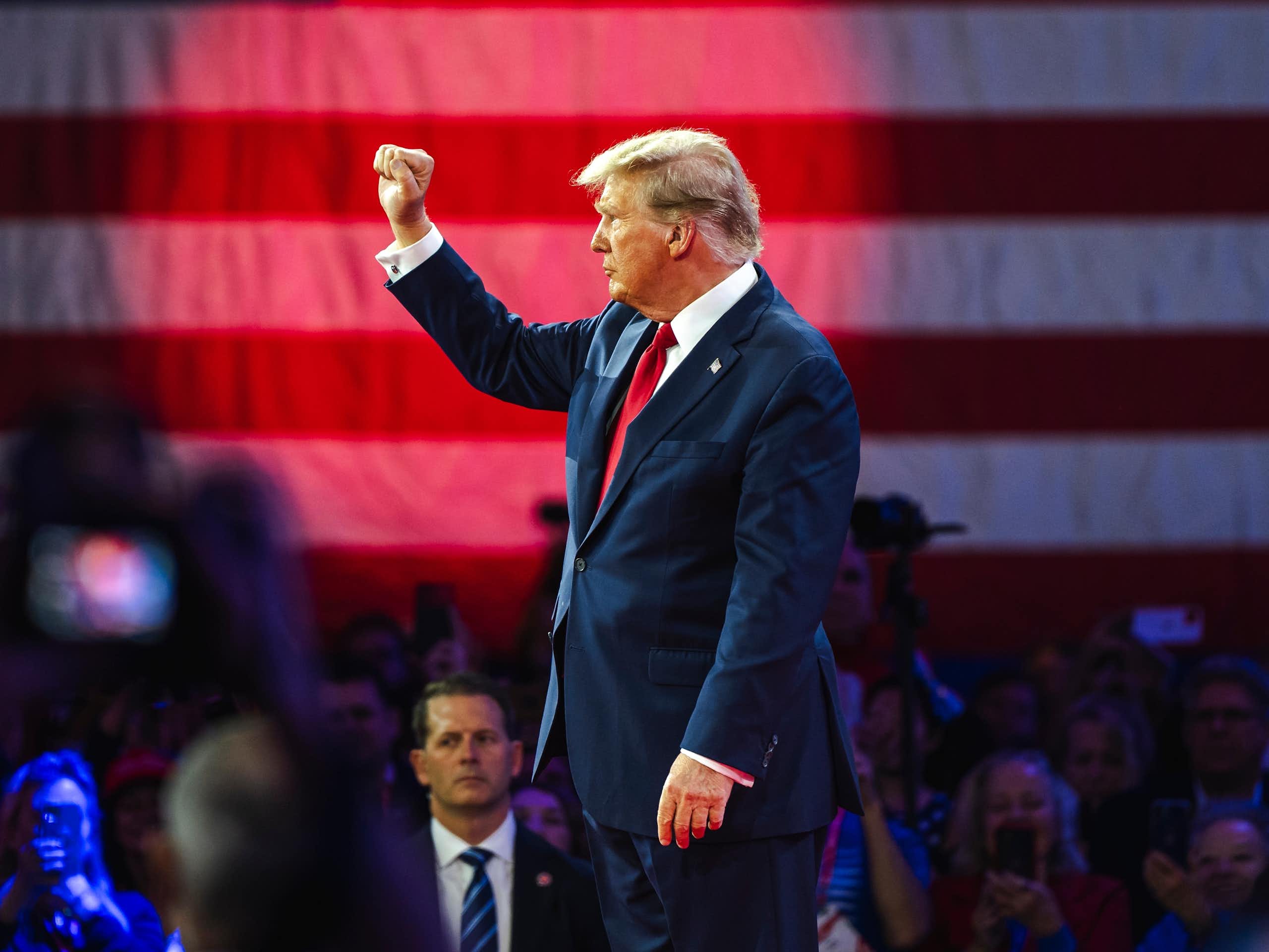 Donald Trump standing in front of a crowd with his fist raised.