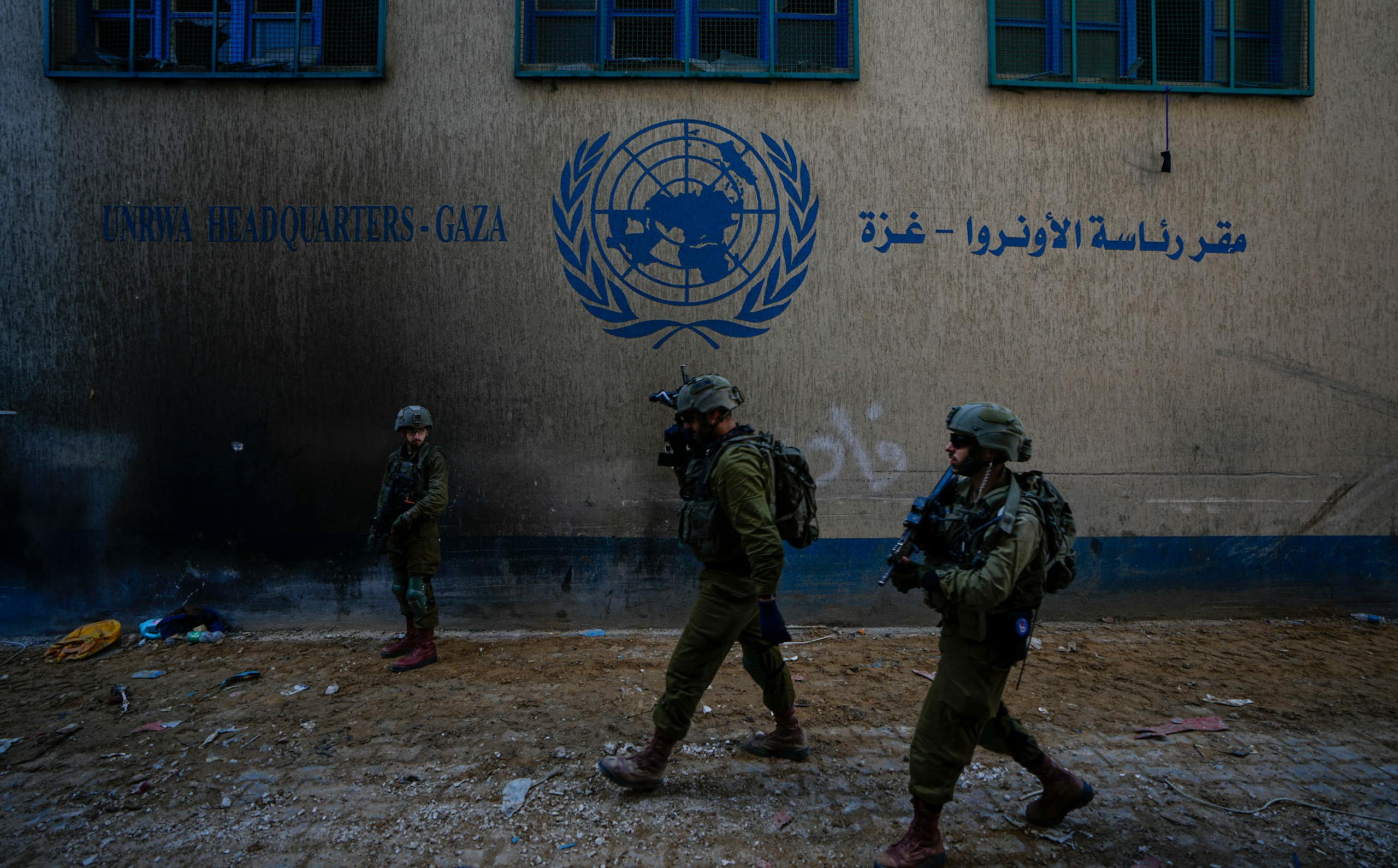 Soldiers in fatigues and helmets walk past a building with a UN logo on it.