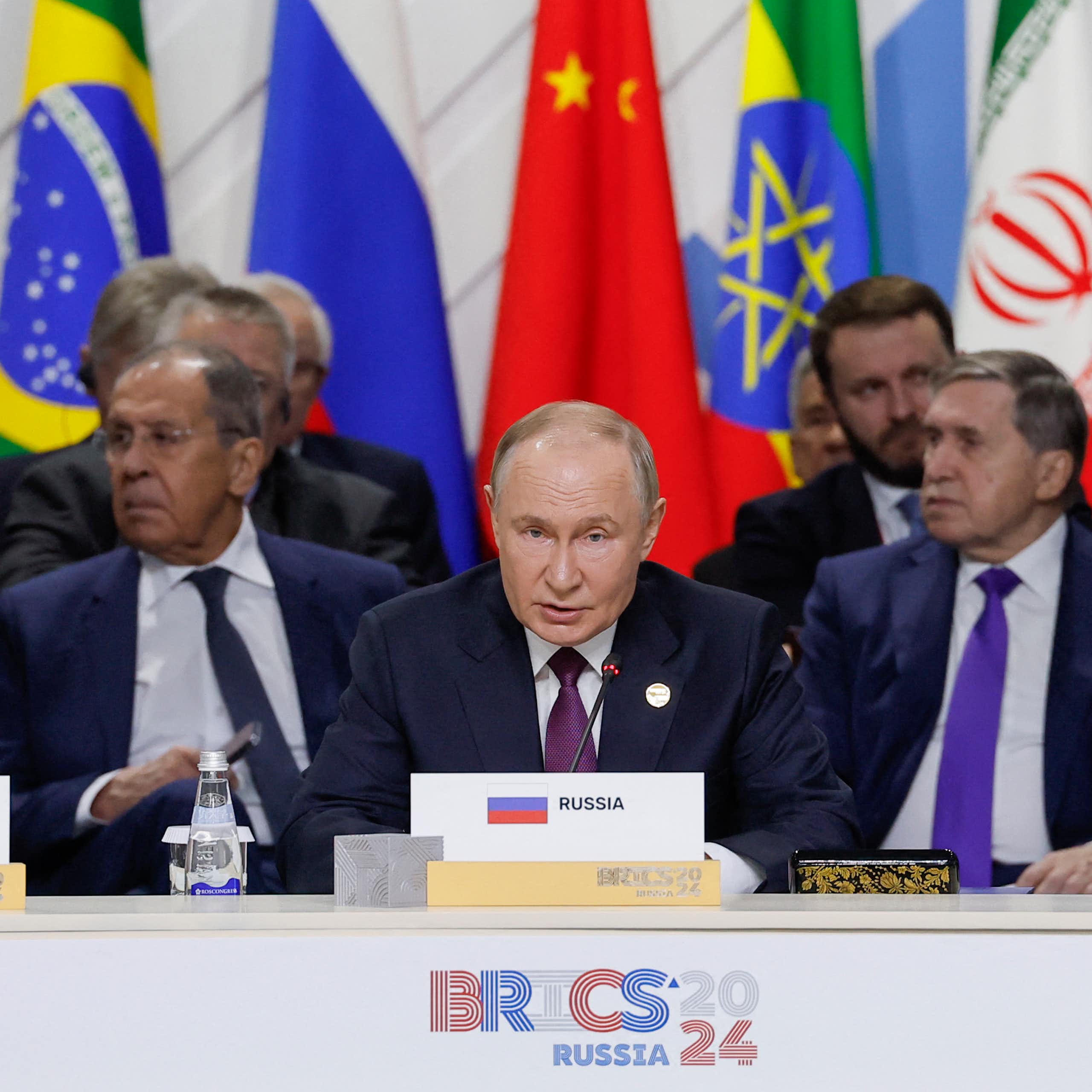 Men seated at a desk with national flags behind them