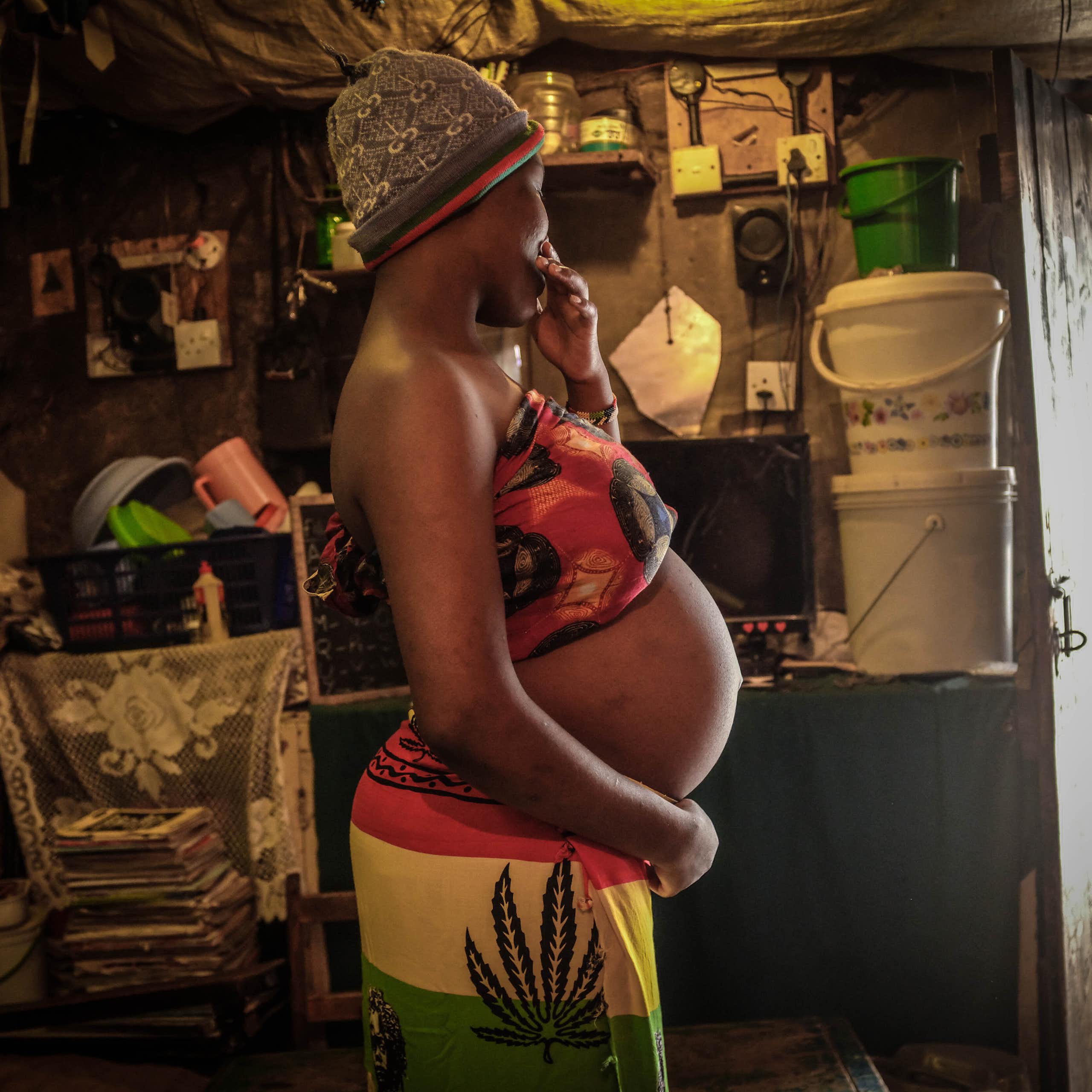 A heavily pregnant young woman, turned away from the camera, gently holds her belly with one hand