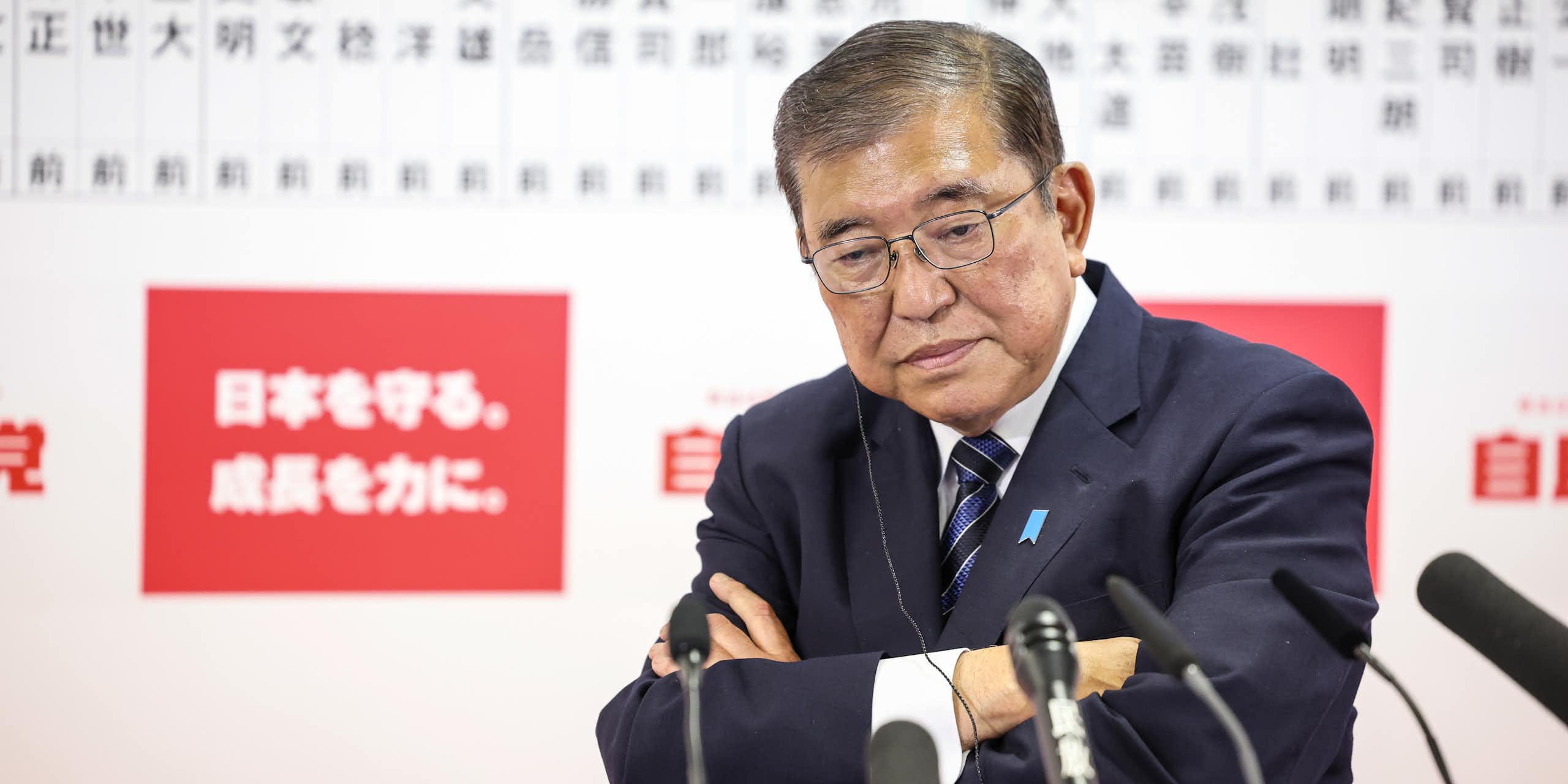 Shigeru Ishiba addressing the media with his arms crossed and a glum look on his face.