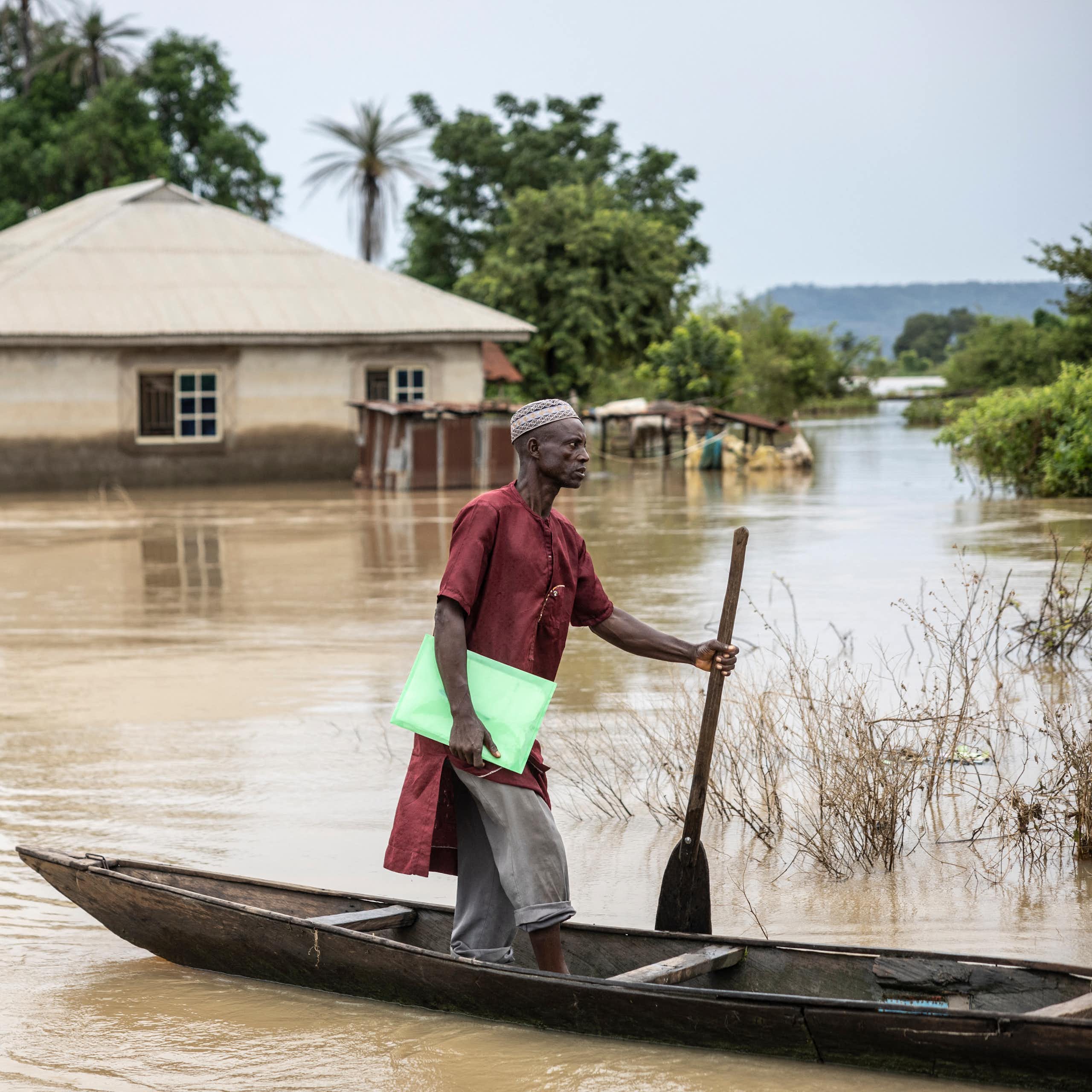 A man standing on a canoe surrounded by flood waters