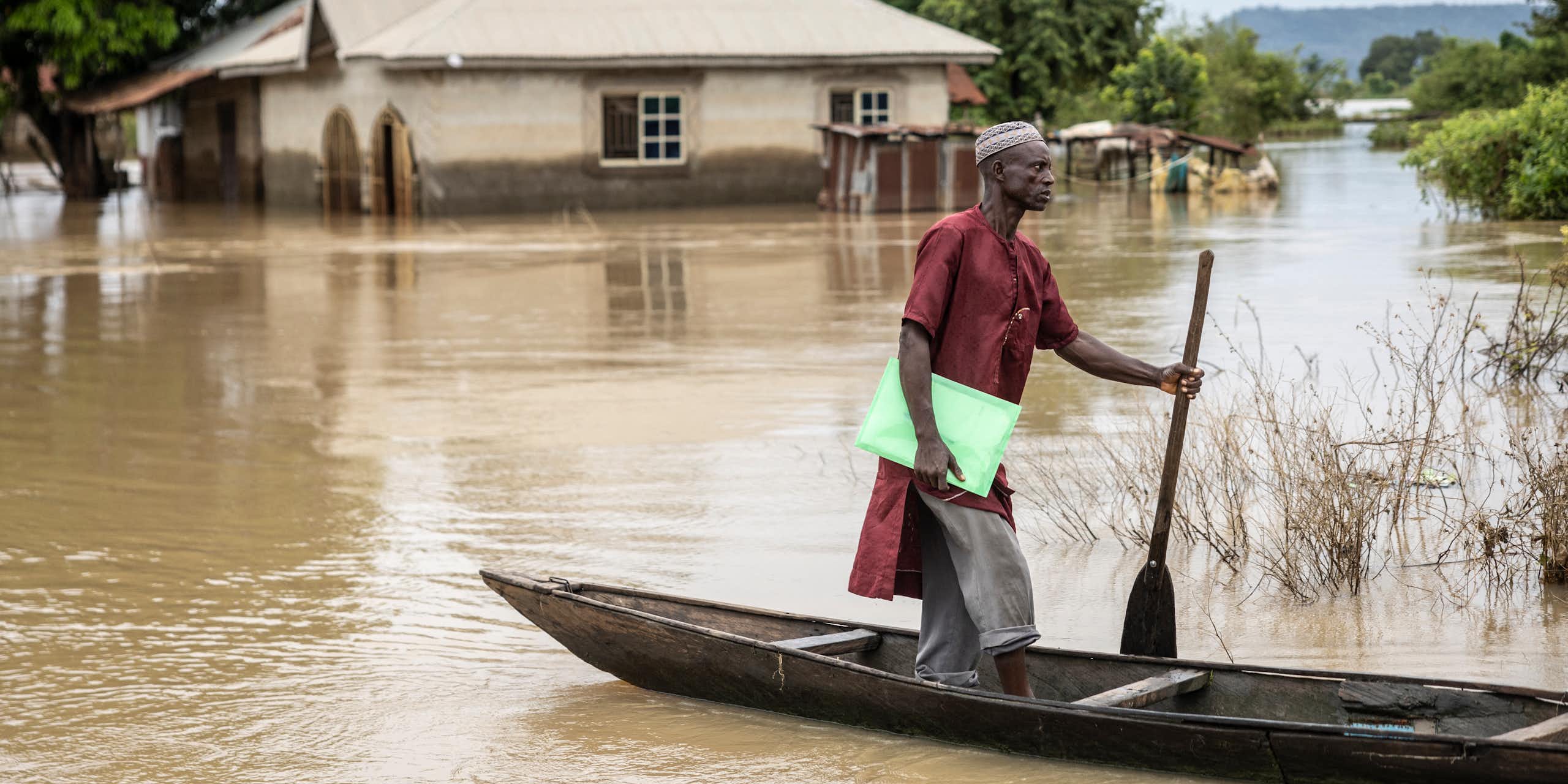 A man standing on a canoe surrounded by flood waters