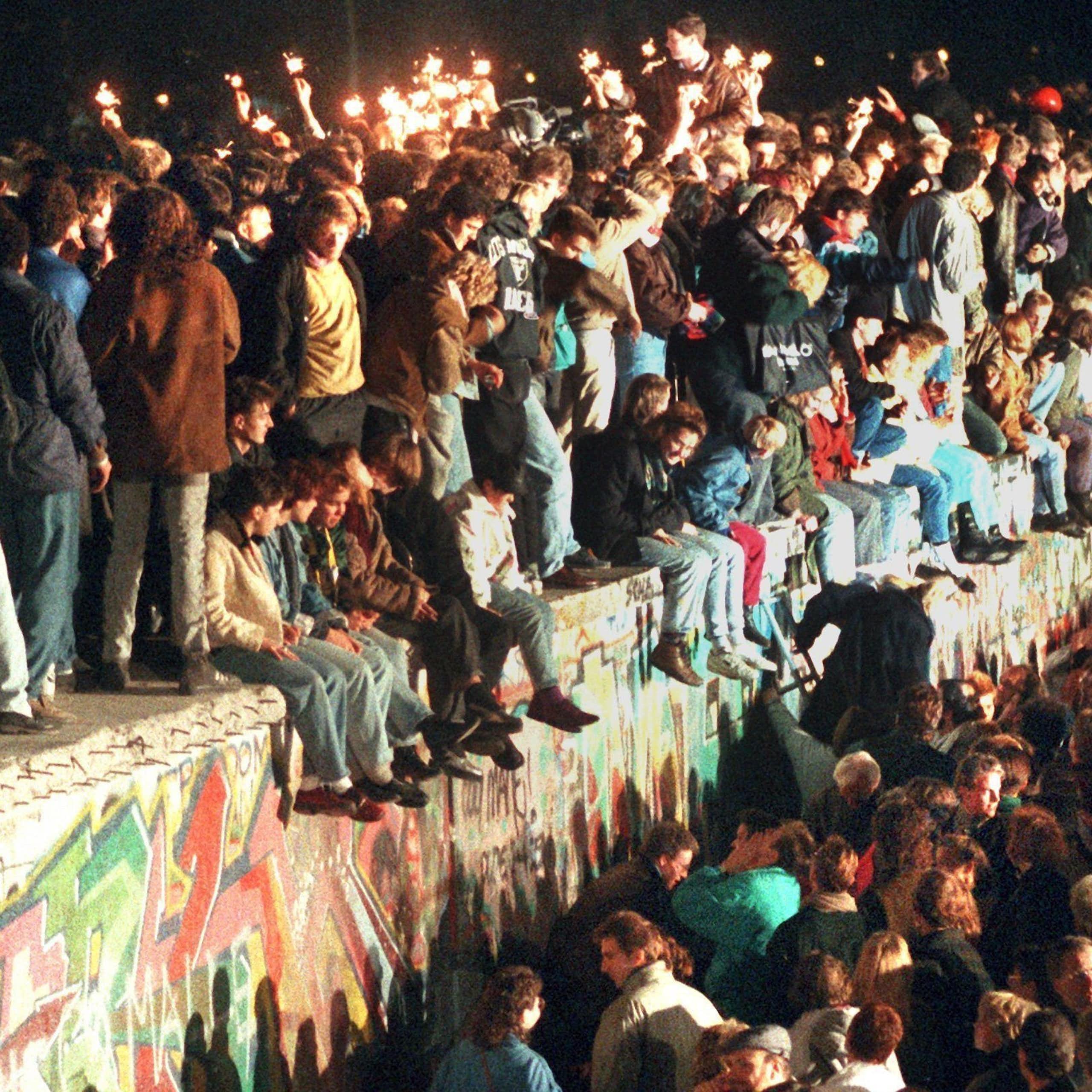 A historical photo of people standing and sitting on the Berlin wall as it is about to be torn down.