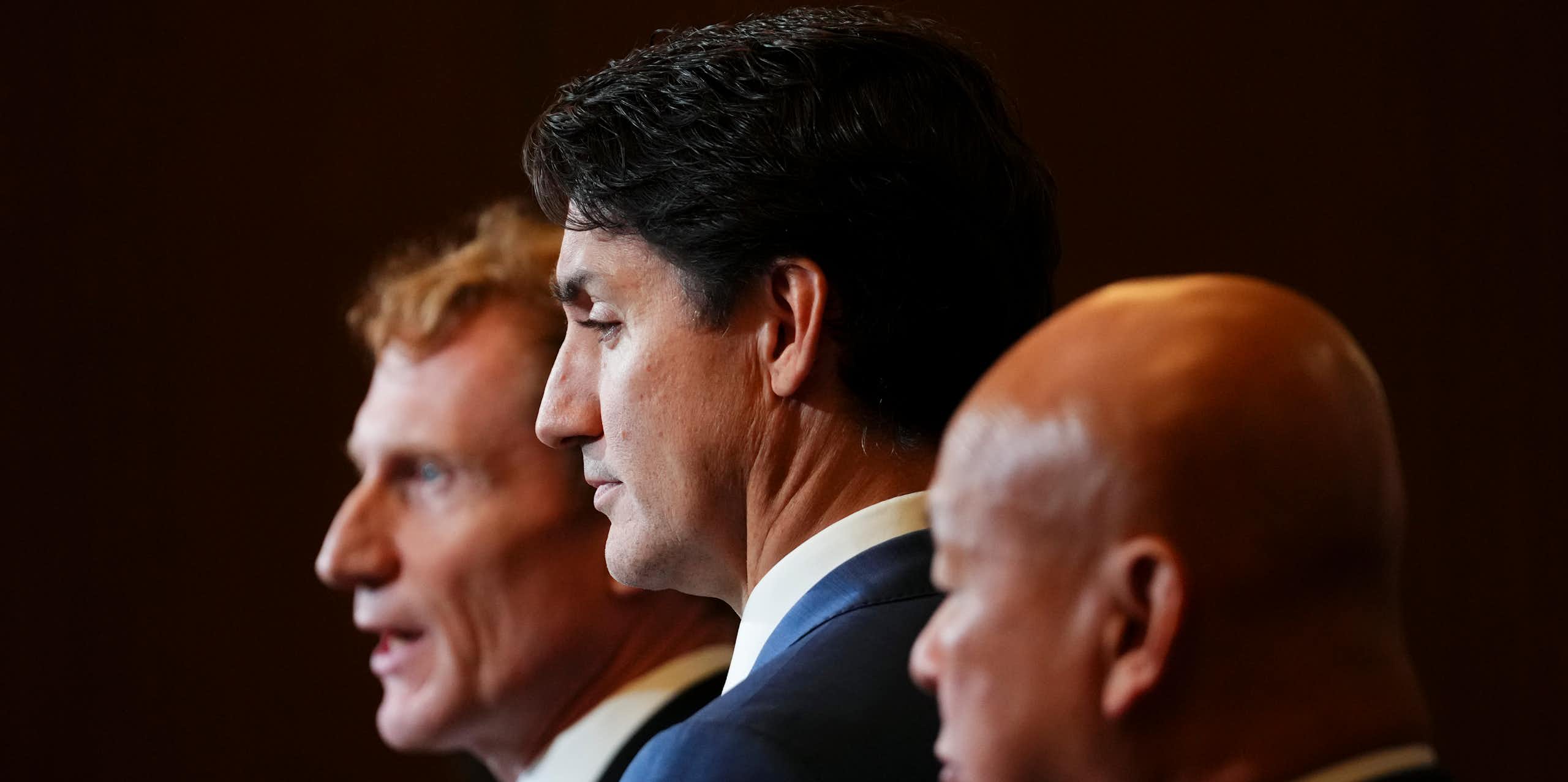 Three middle aged men in dark suits stand next to each other