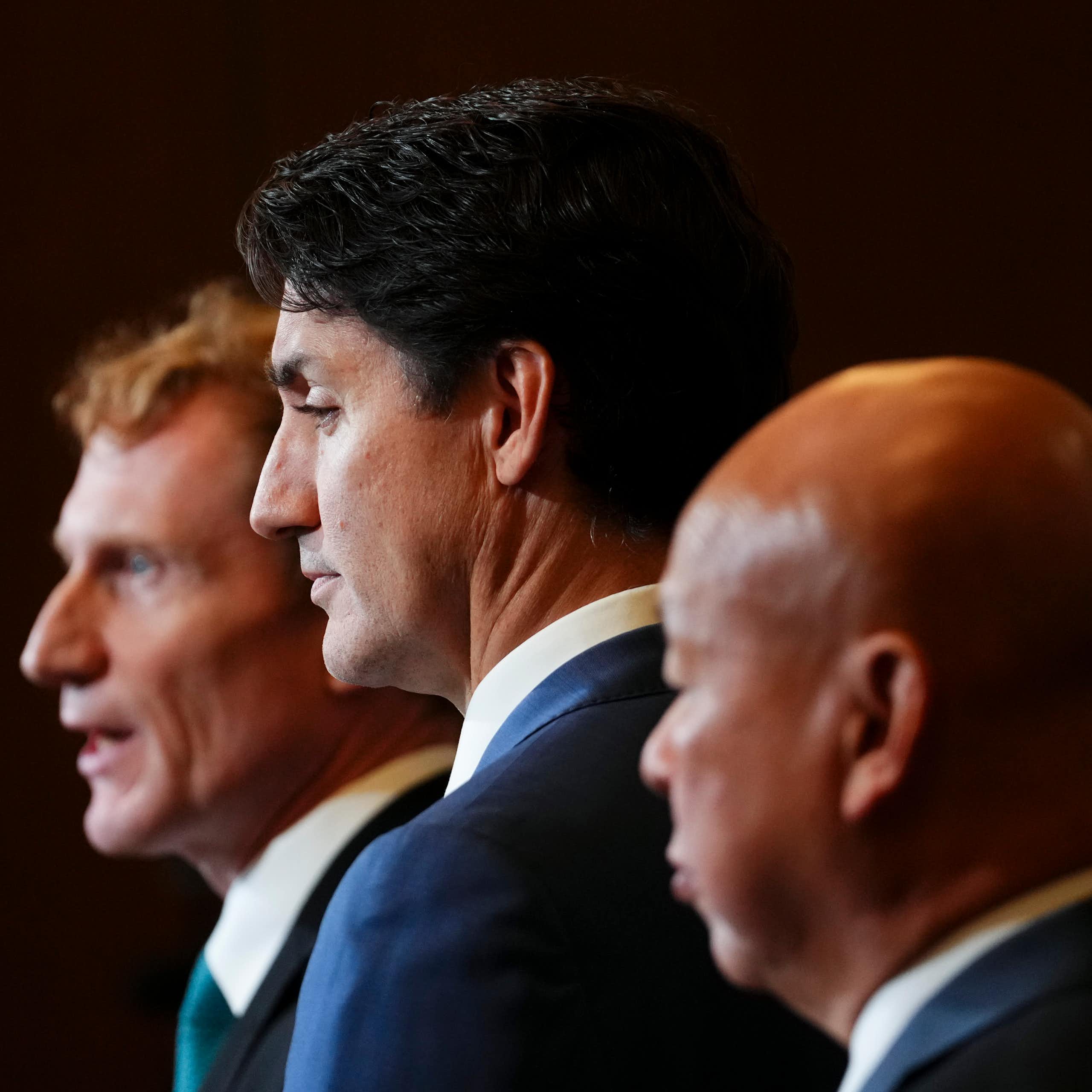 Three middle aged men in dark suits stand next to each other