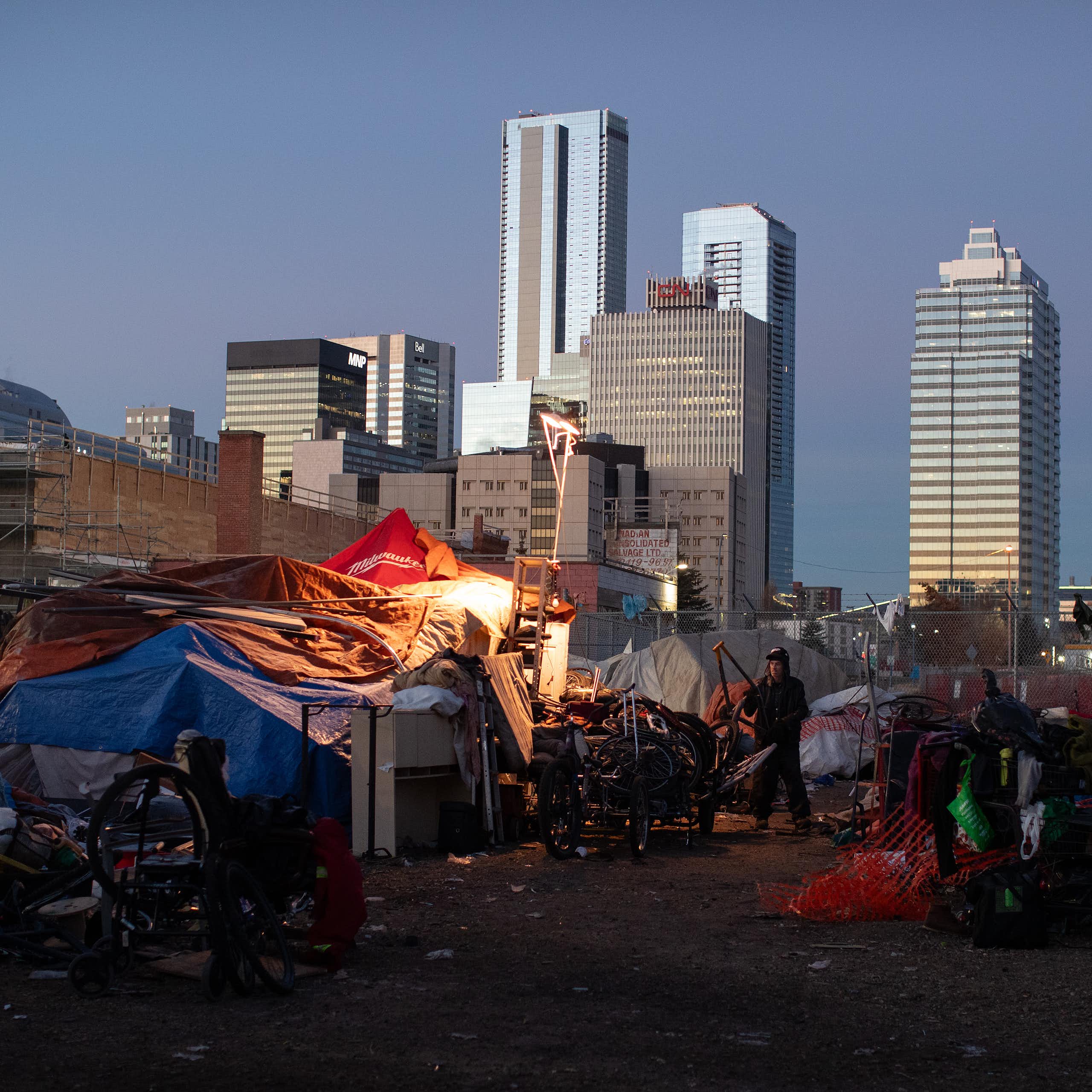 Tents at an encampment, tall glass buildings in the background